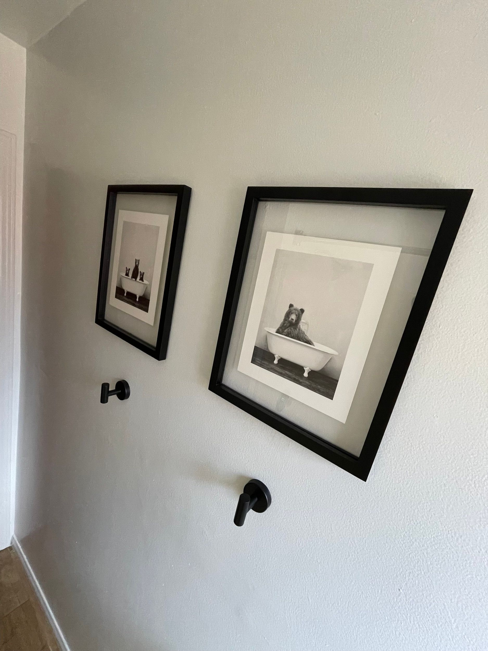 Two framed black and white photos on a white wall, and two black hooks below them.