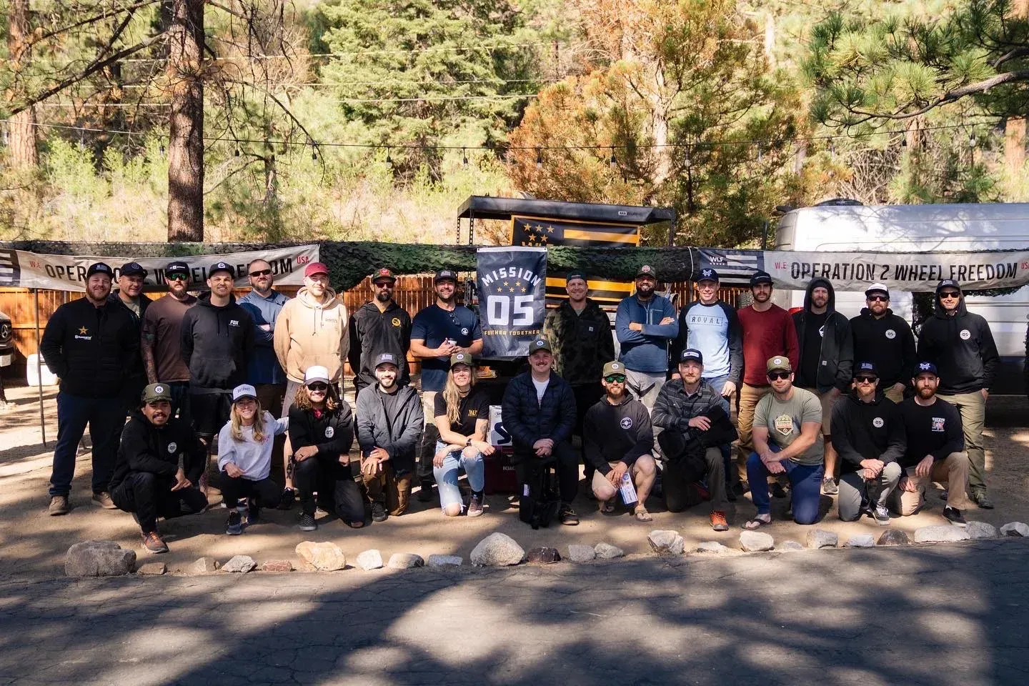 Group photo of people outdoors in front of a rustic building and forest.