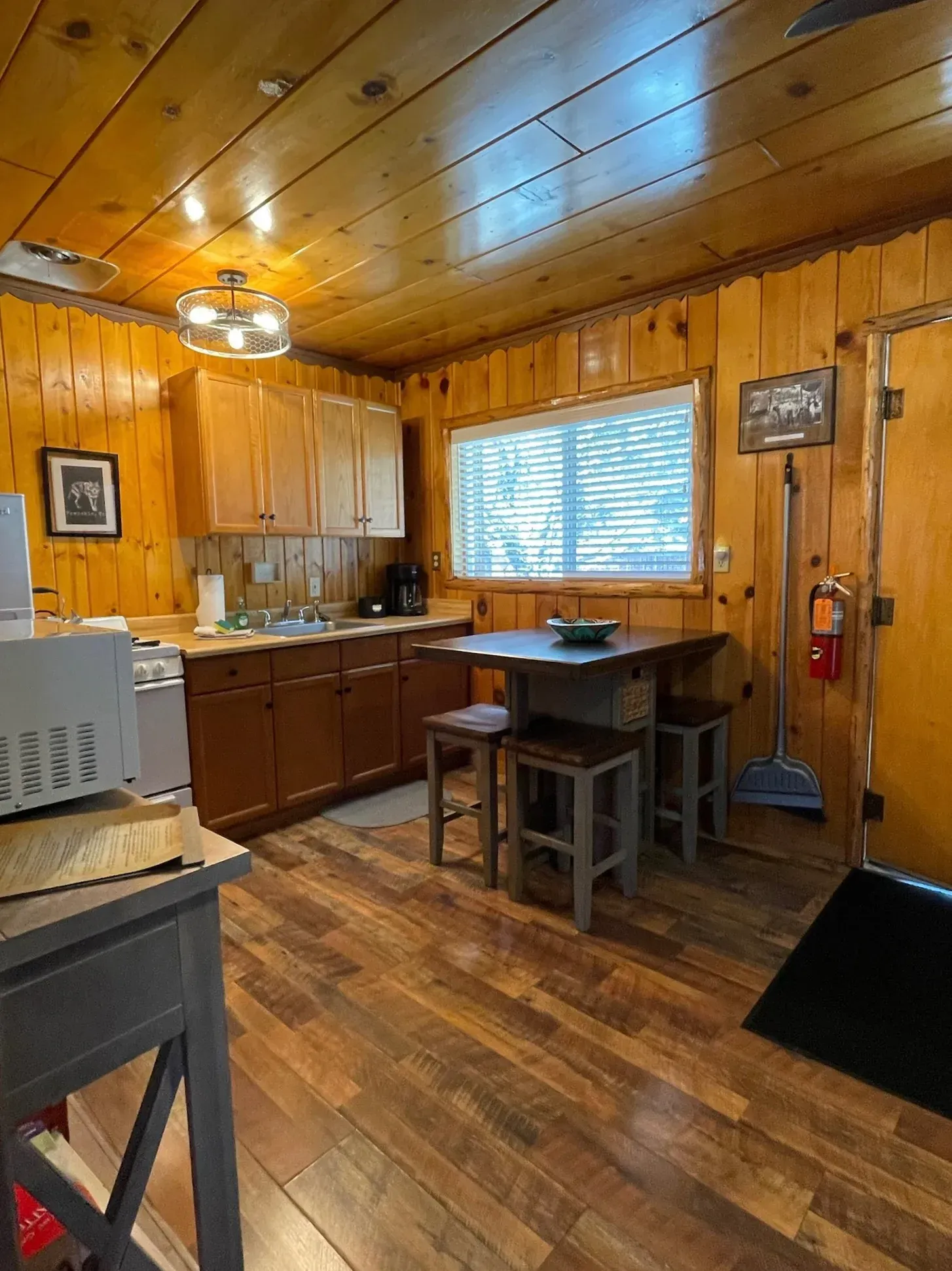 Cozy cabin kitchen with wood paneling, cabinets, and a small table with stools.