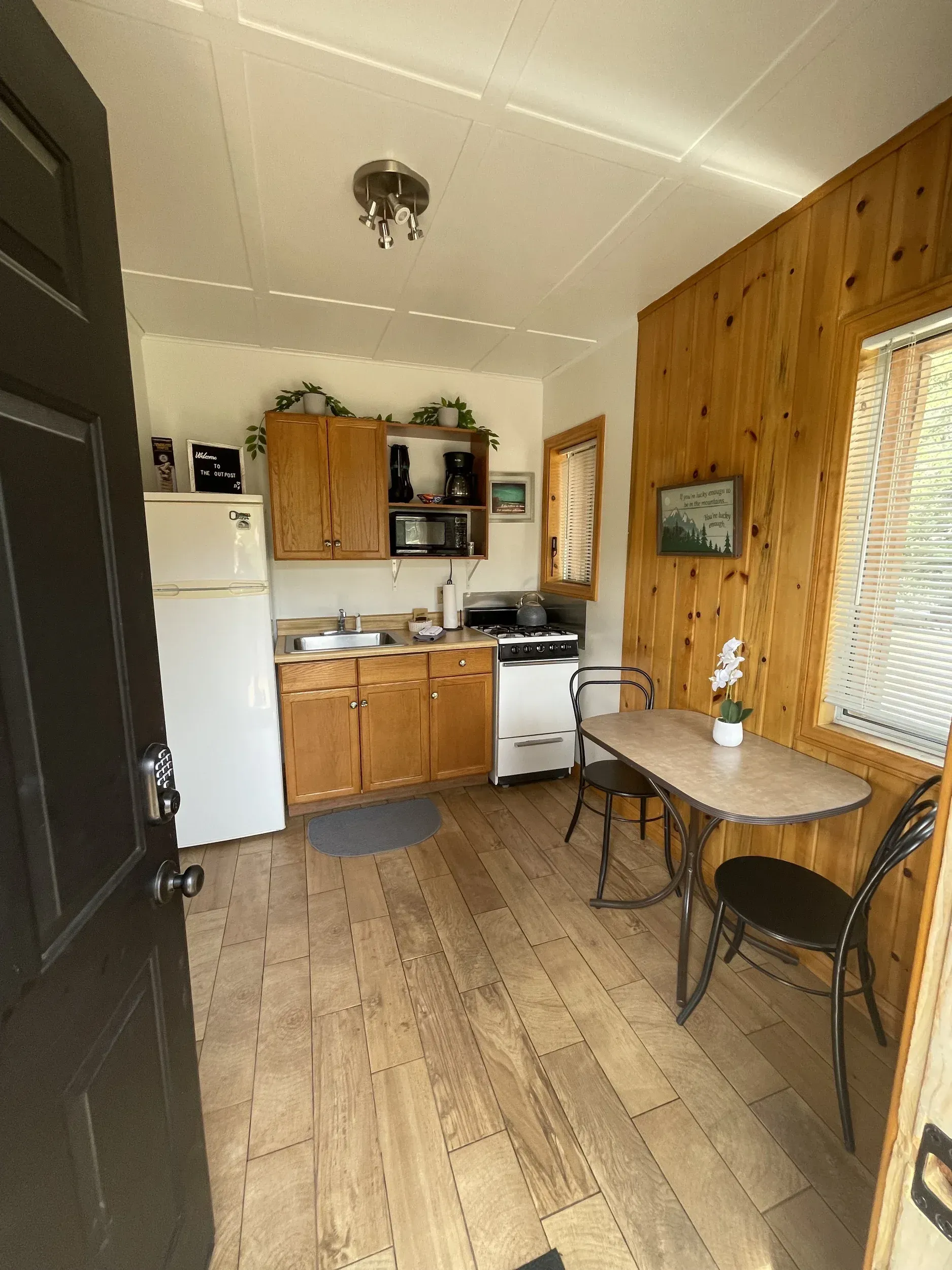 Small cabin kitchen with refrigerator, cabinets, stove, table, and two chairs.