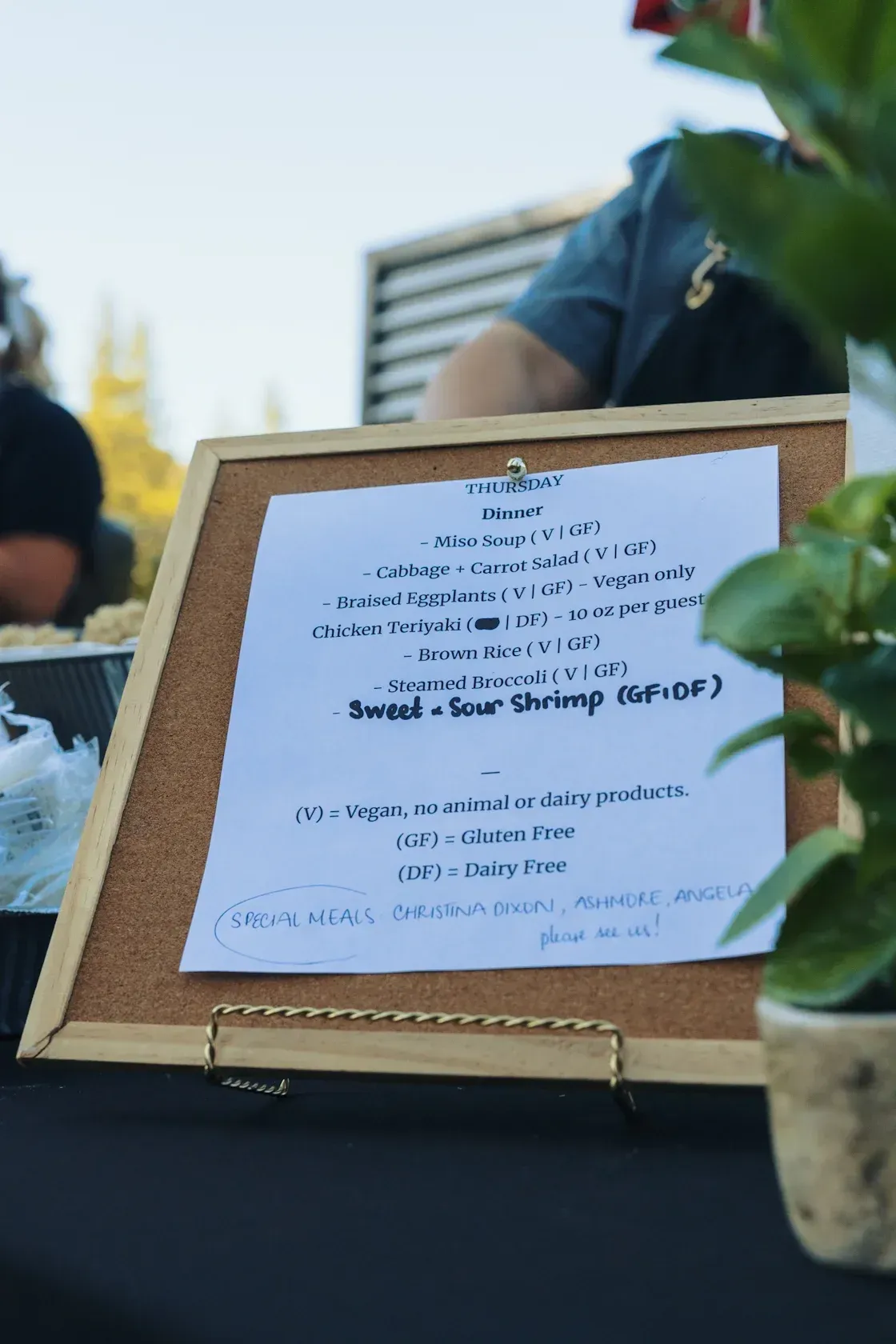 Menu board on easel, Sweet & Sour Shrimp (GF/DF) highlighted, food stall outdoors.