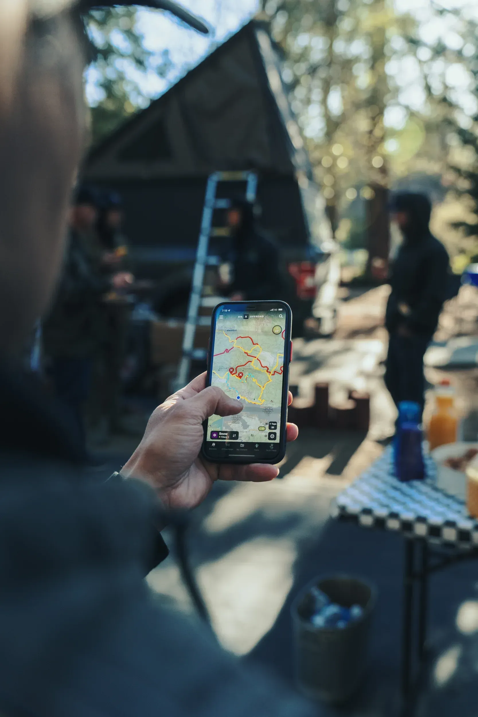 Person holding phone with map app, camping scene in background.