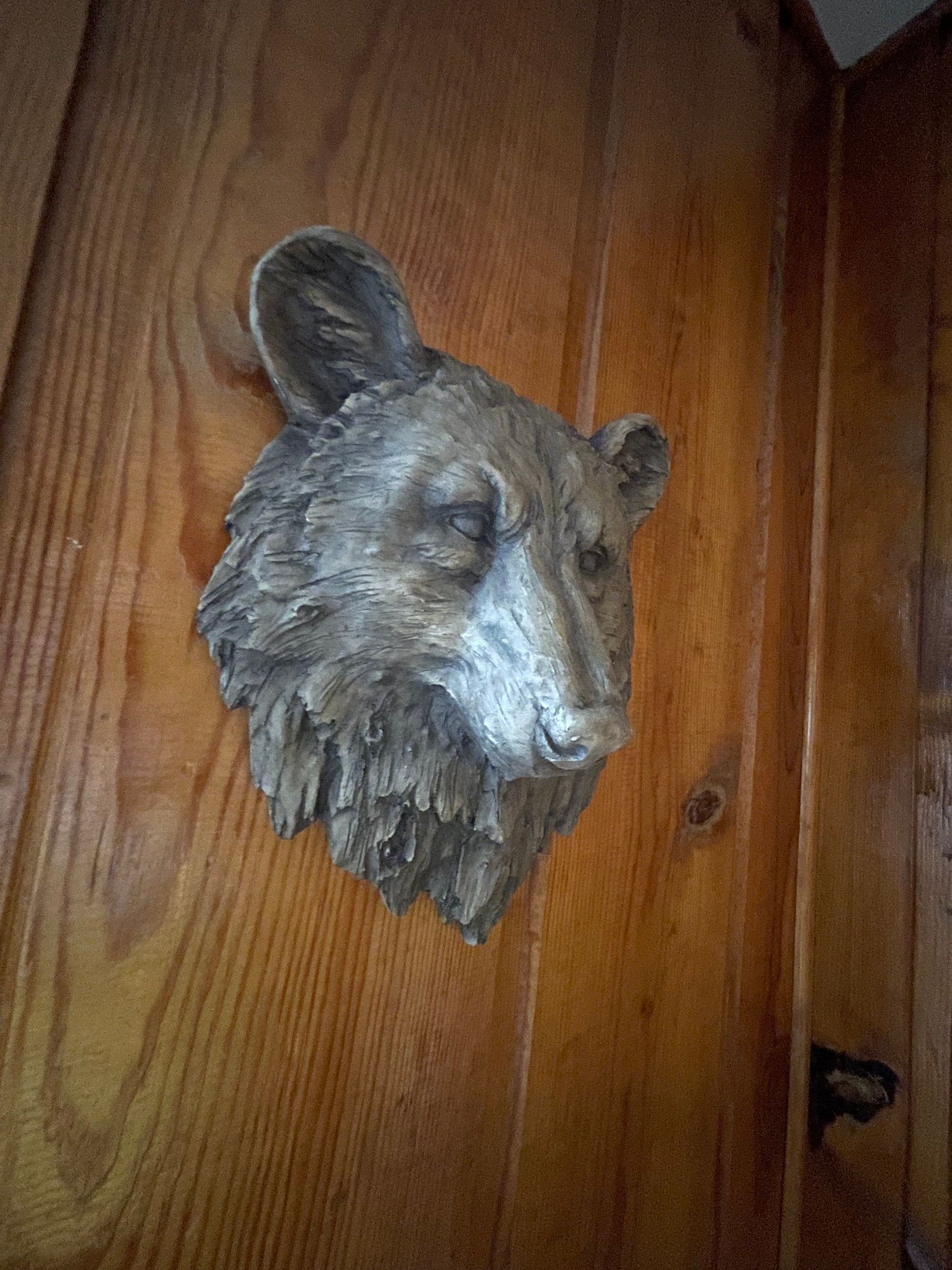 Bear head sculpture mounted on a wooden surface, with detailed fur and a neutral expression.
