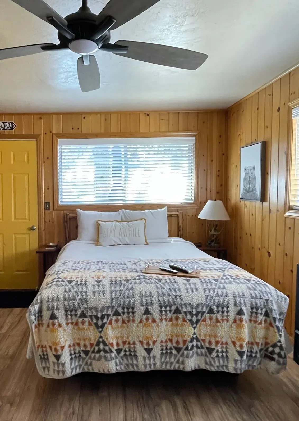 Bedroom with a double bed, wooden walls, a ceiling fan, and a yellow door.