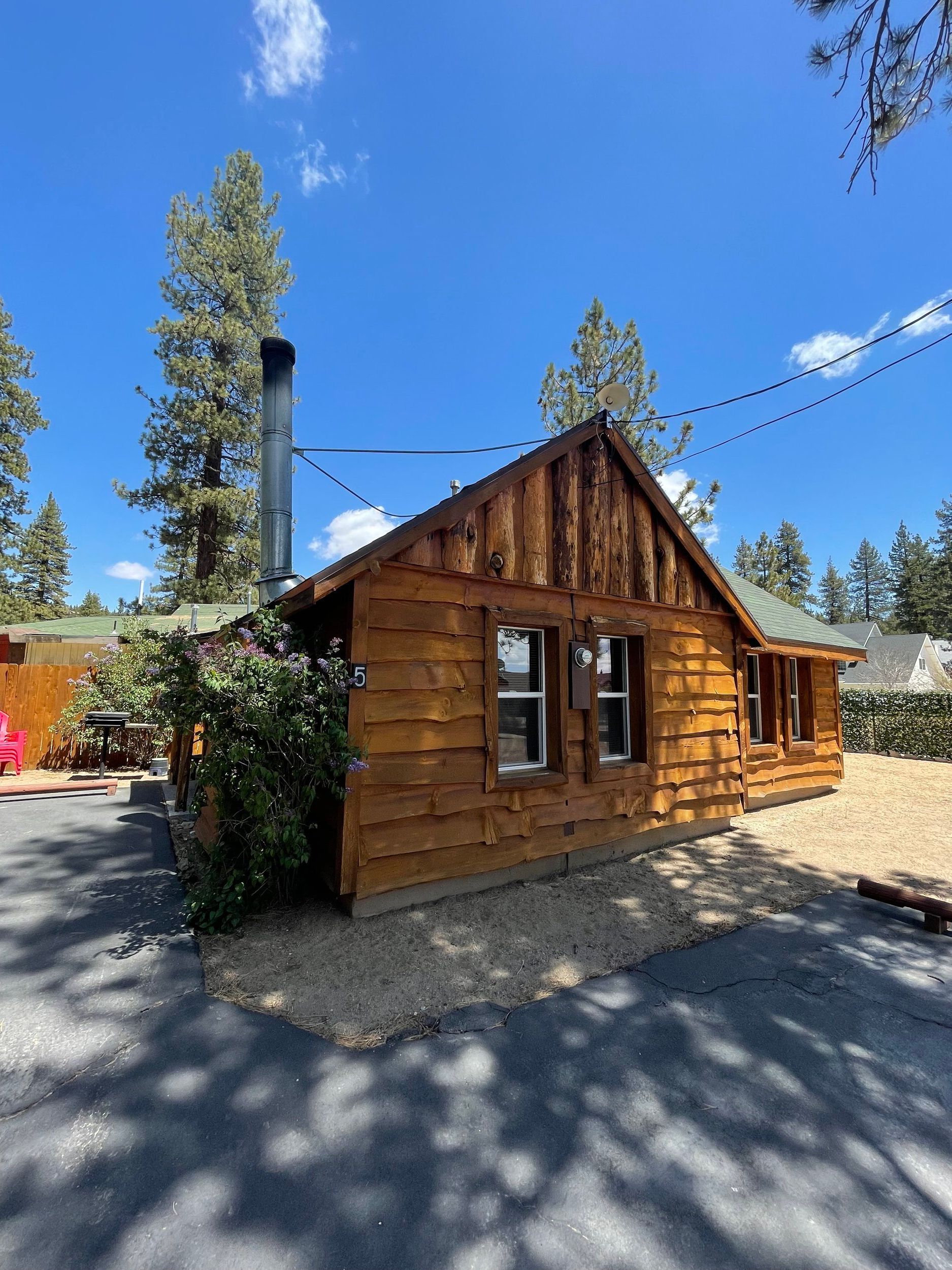 Wooden cabin with a dark chimney, two windows, and gravel driveway under a blue sky.