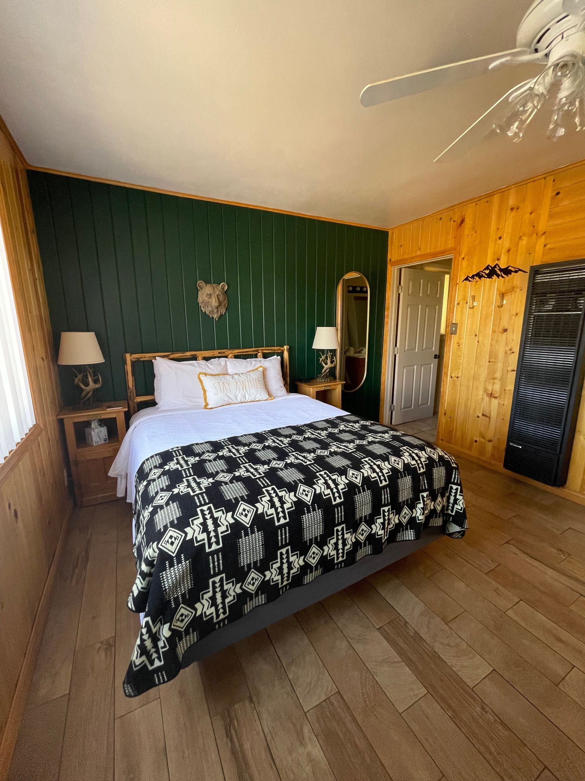 Bedroom with wooden walls, bed with patterned cover, green accent wall, and ceiling fan.