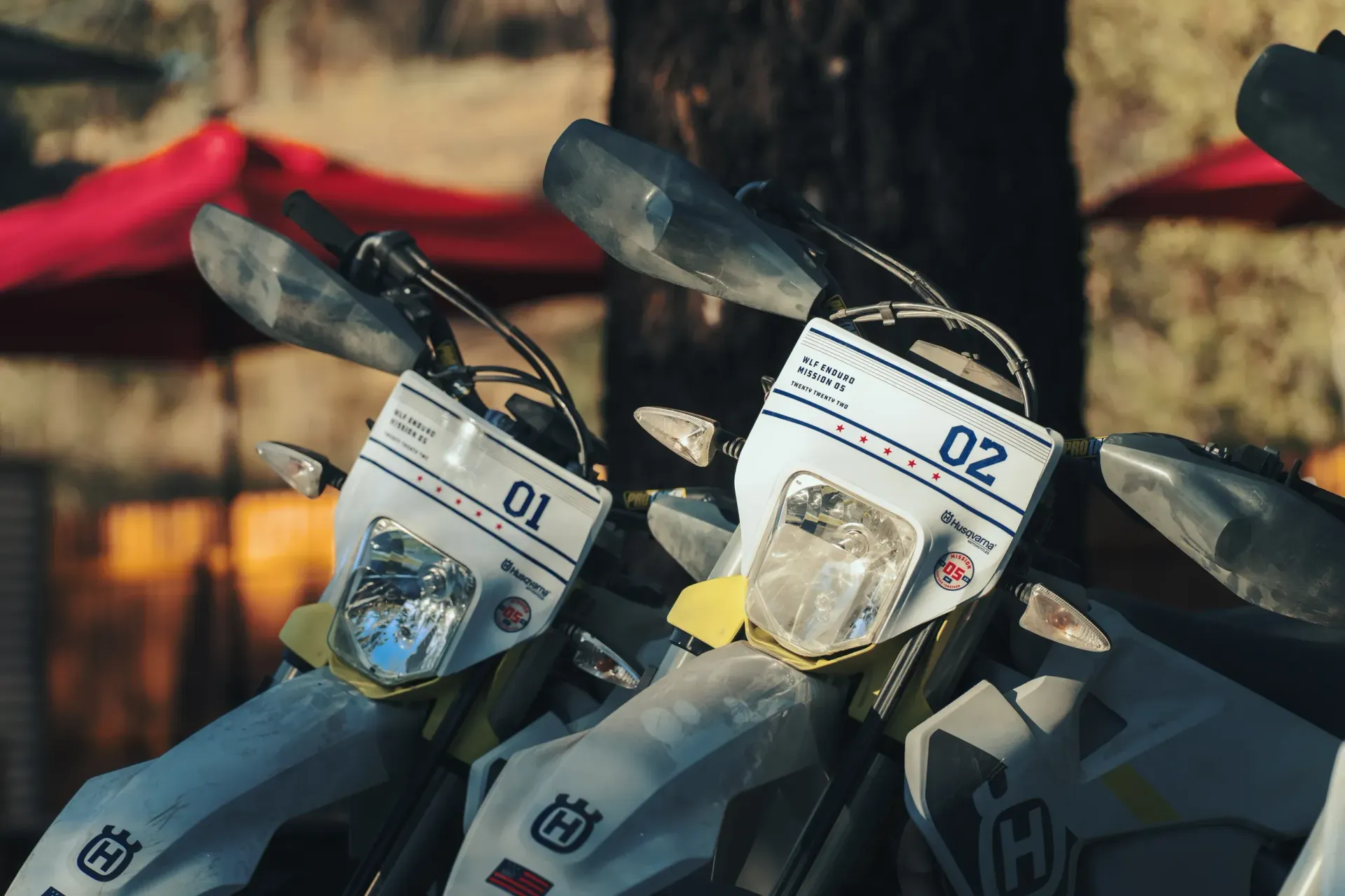 Two white Husqvarna motorcycles with the numbers 01 and 02 on them.