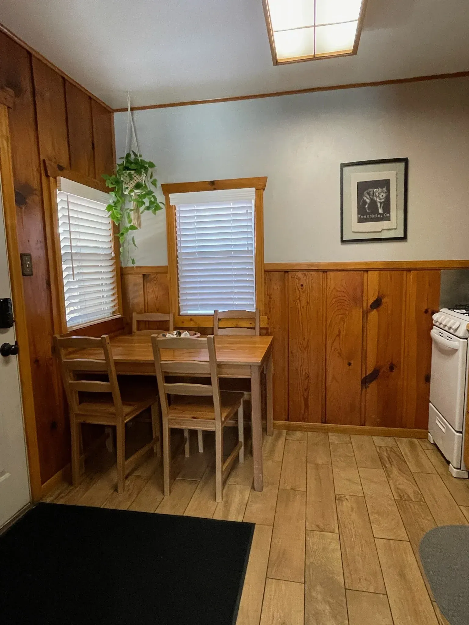 Dining area with wooden table and chairs, wood-paneled walls, and a hanging plant.