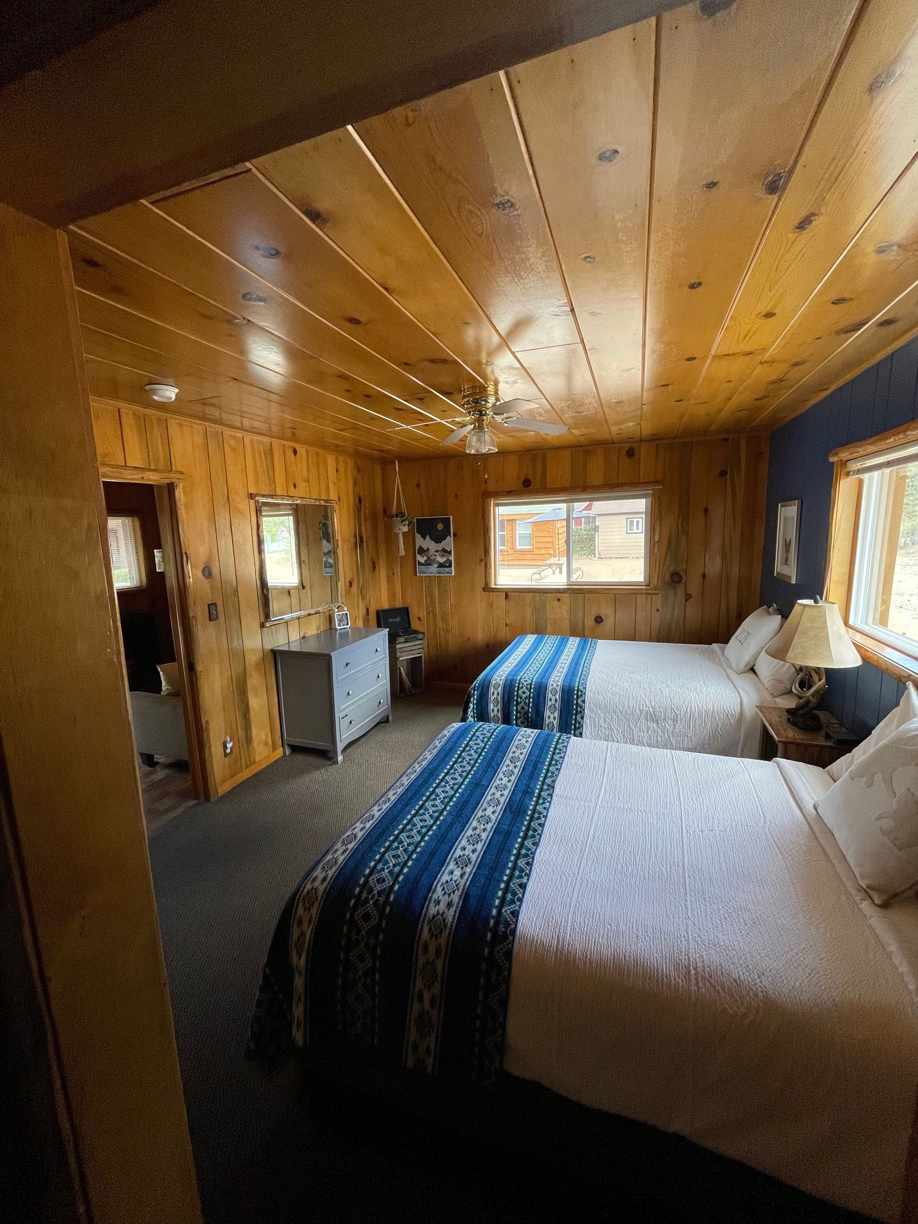 Bedroom with two beds, wood paneling, small window, and a bathroom doorway on the left.