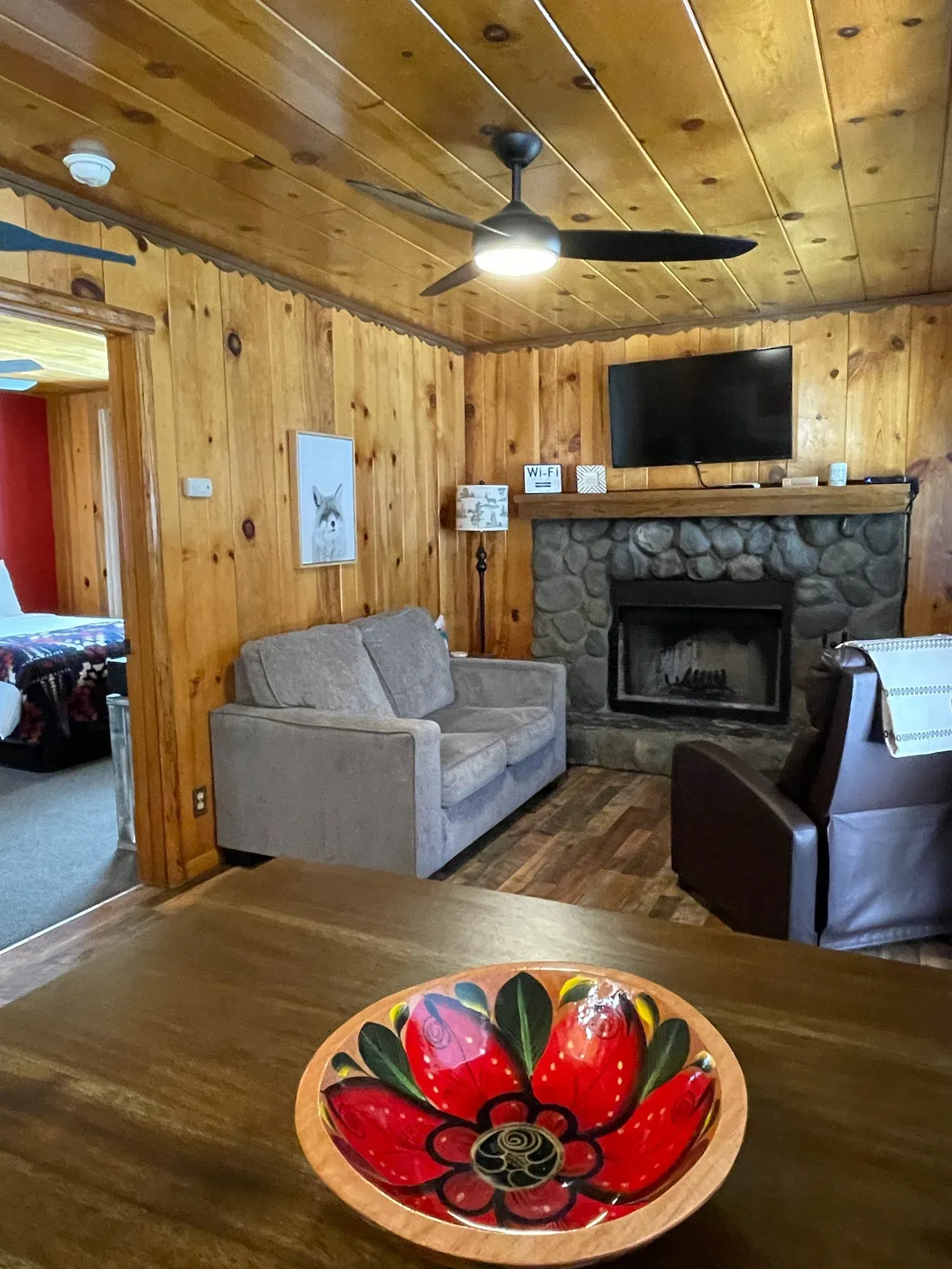 Living room with wood-paneled walls, stone fireplace, and gray couch. A bowl sits in the foreground.