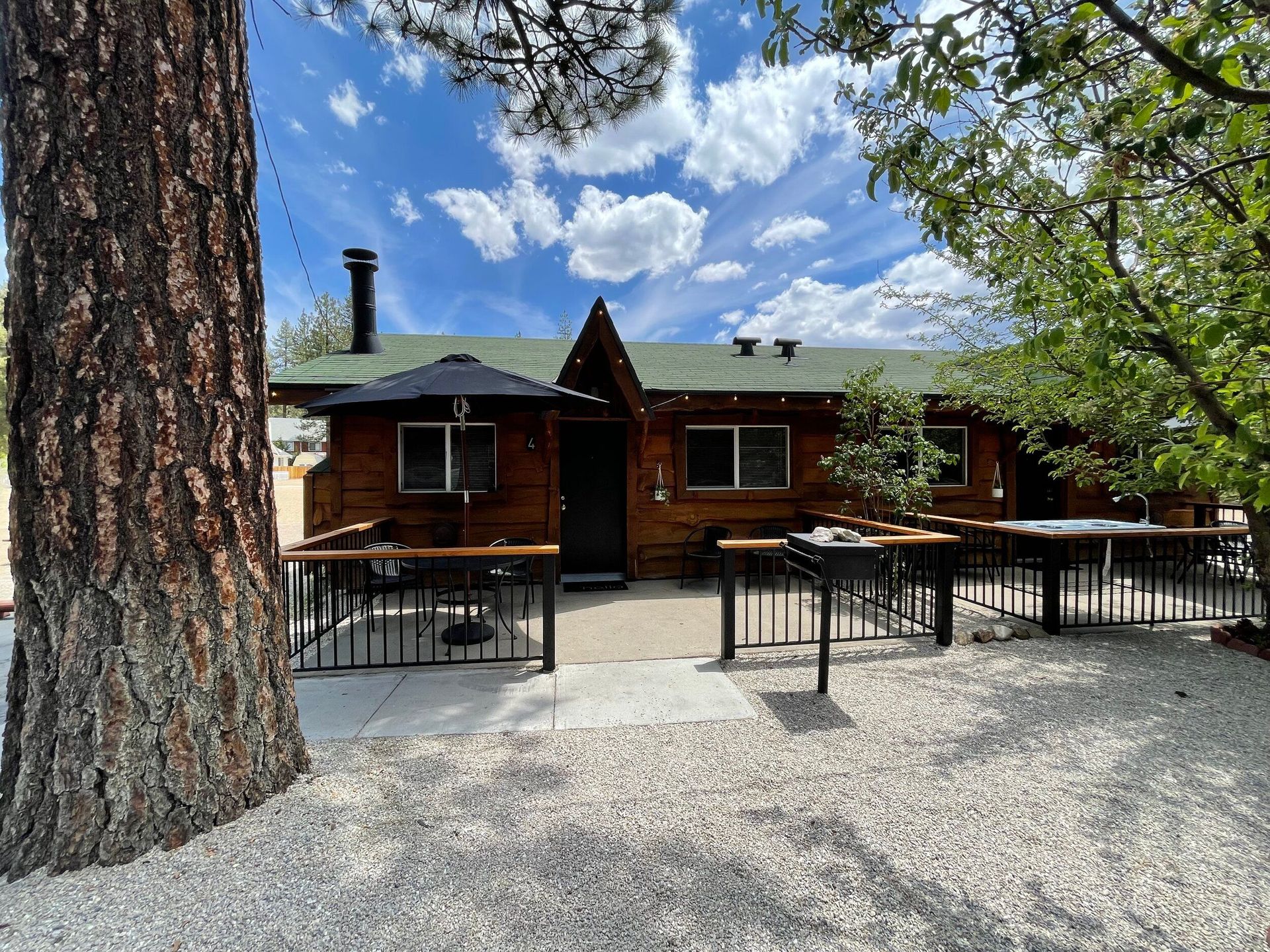 Wooden cabin with a patio and picnic tables under a blue sky with clouds.
