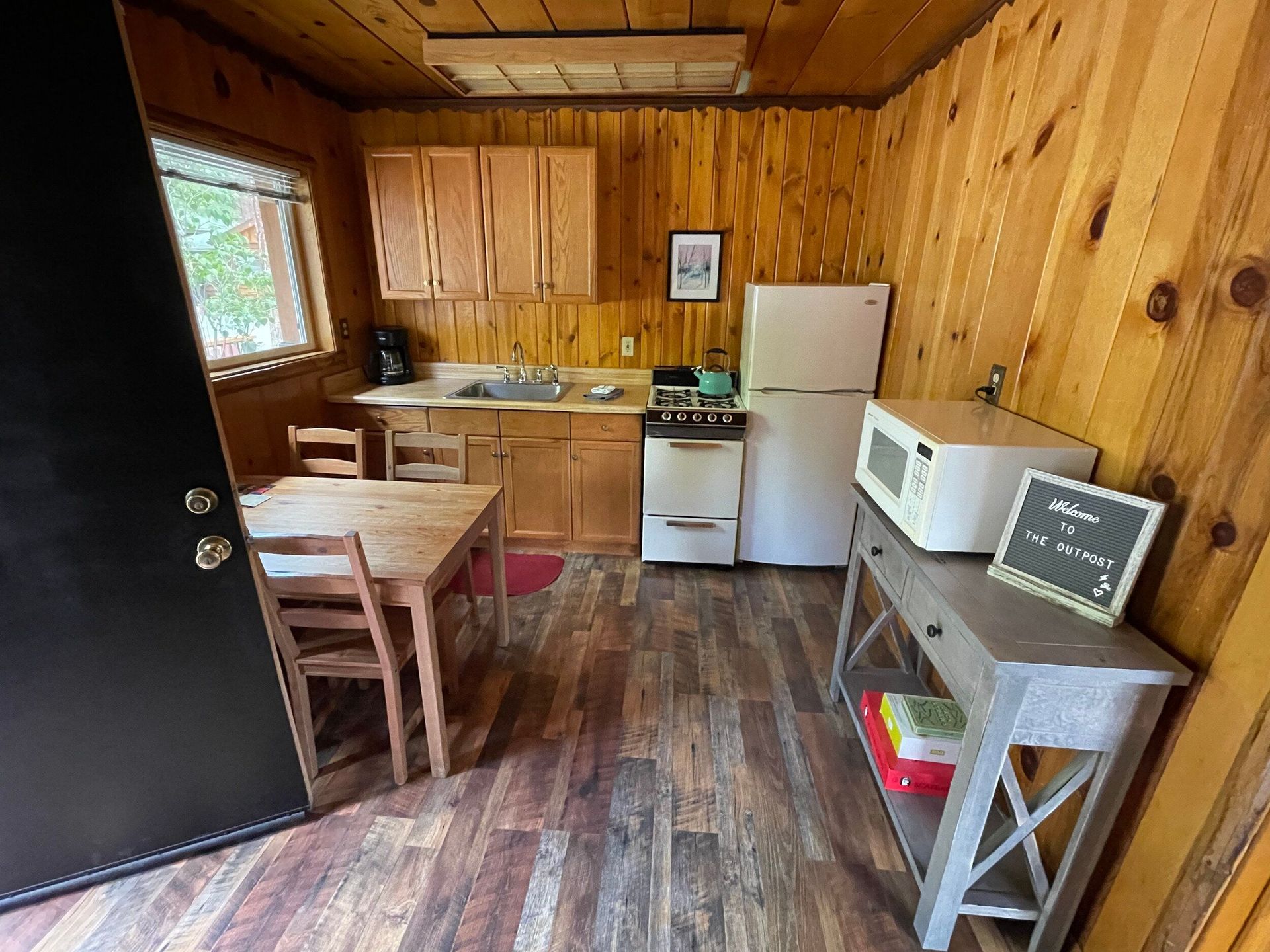Small cabin kitchen with wood paneling, appliances, table, and a black door.