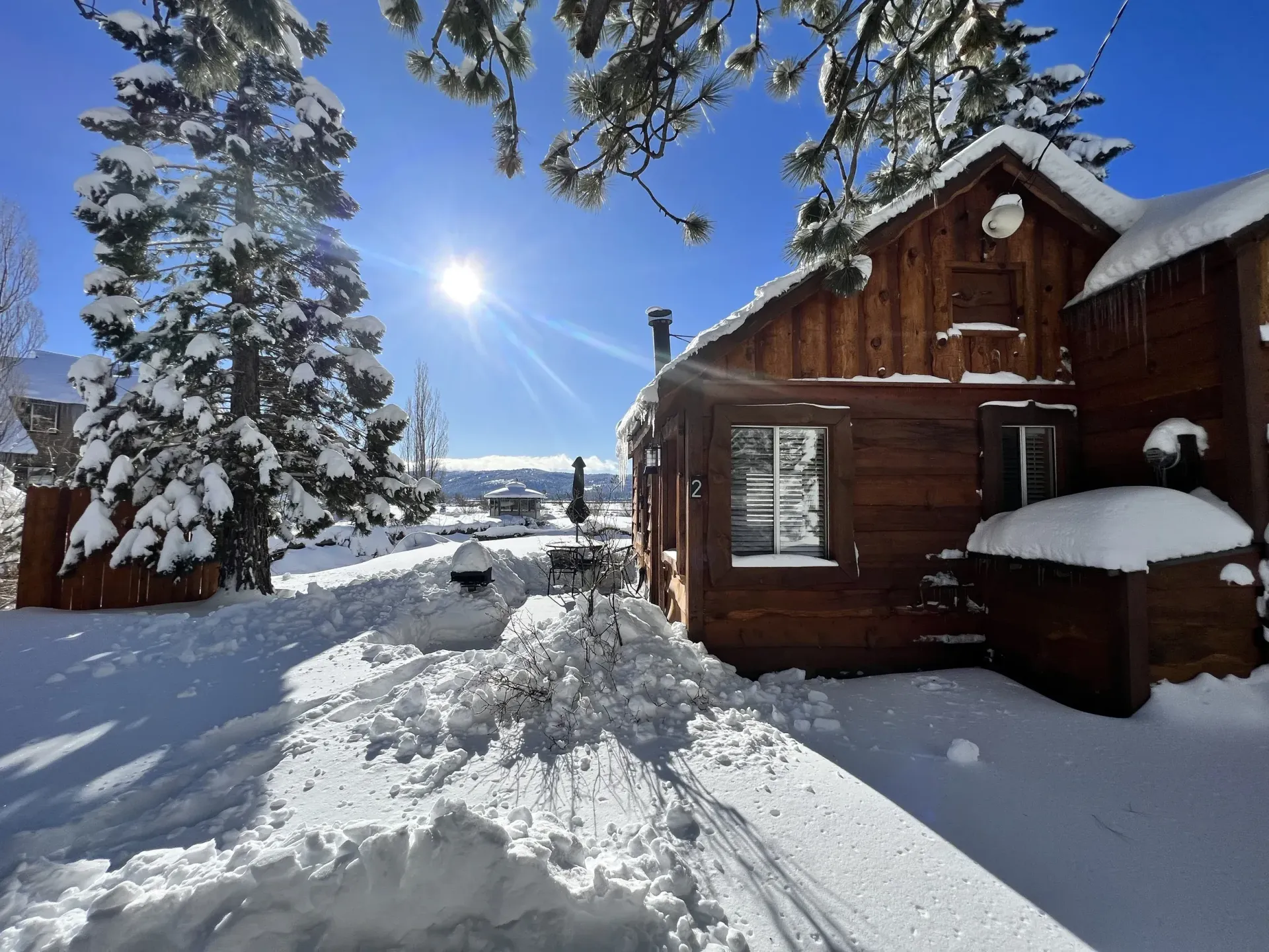 Snow-covered wooden cabin on a bright sunny day; snow drifts and a clear blue sky.
