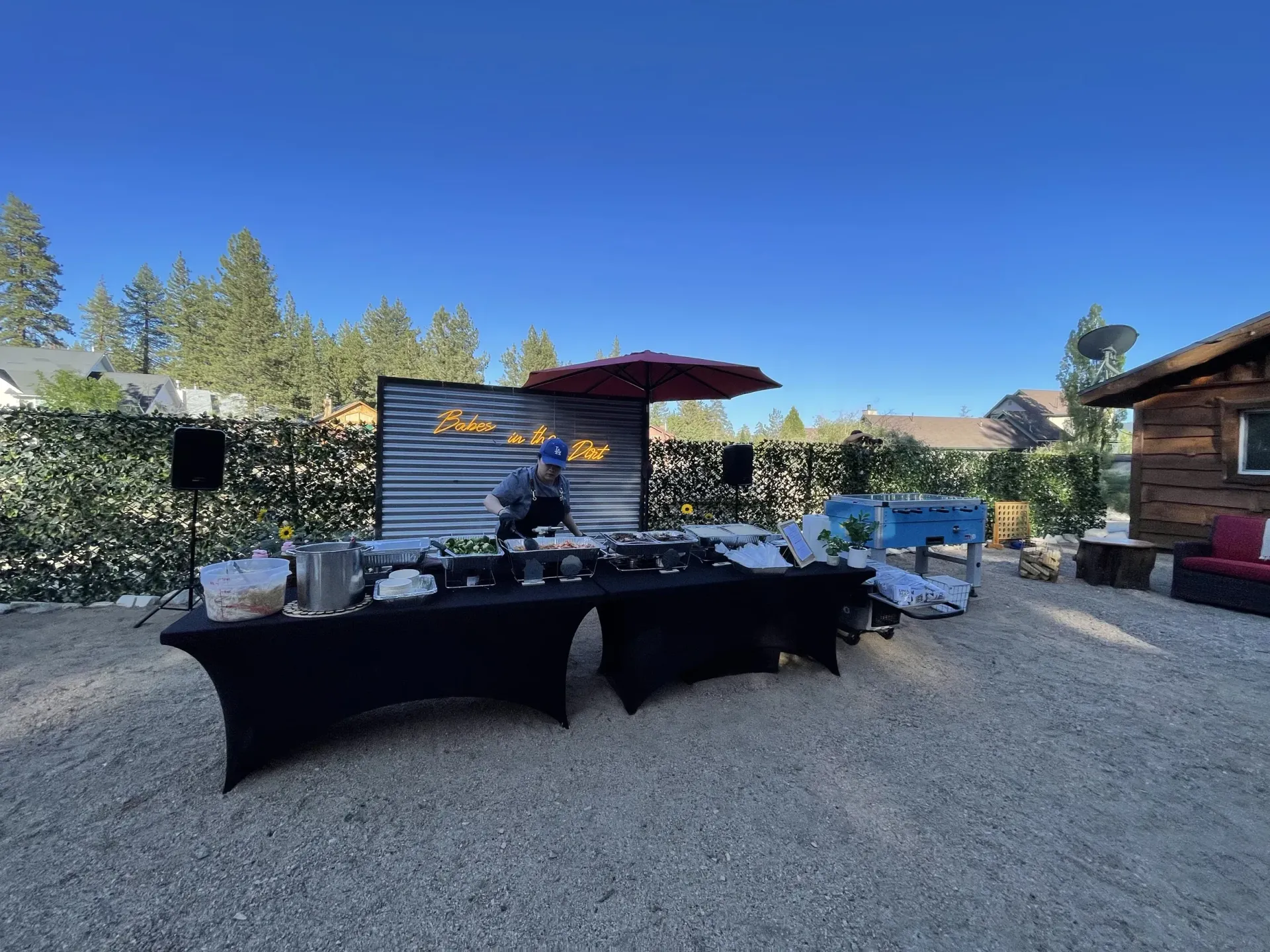 Outdoor event setup with tables, a bar, and decorations under a blue sky.