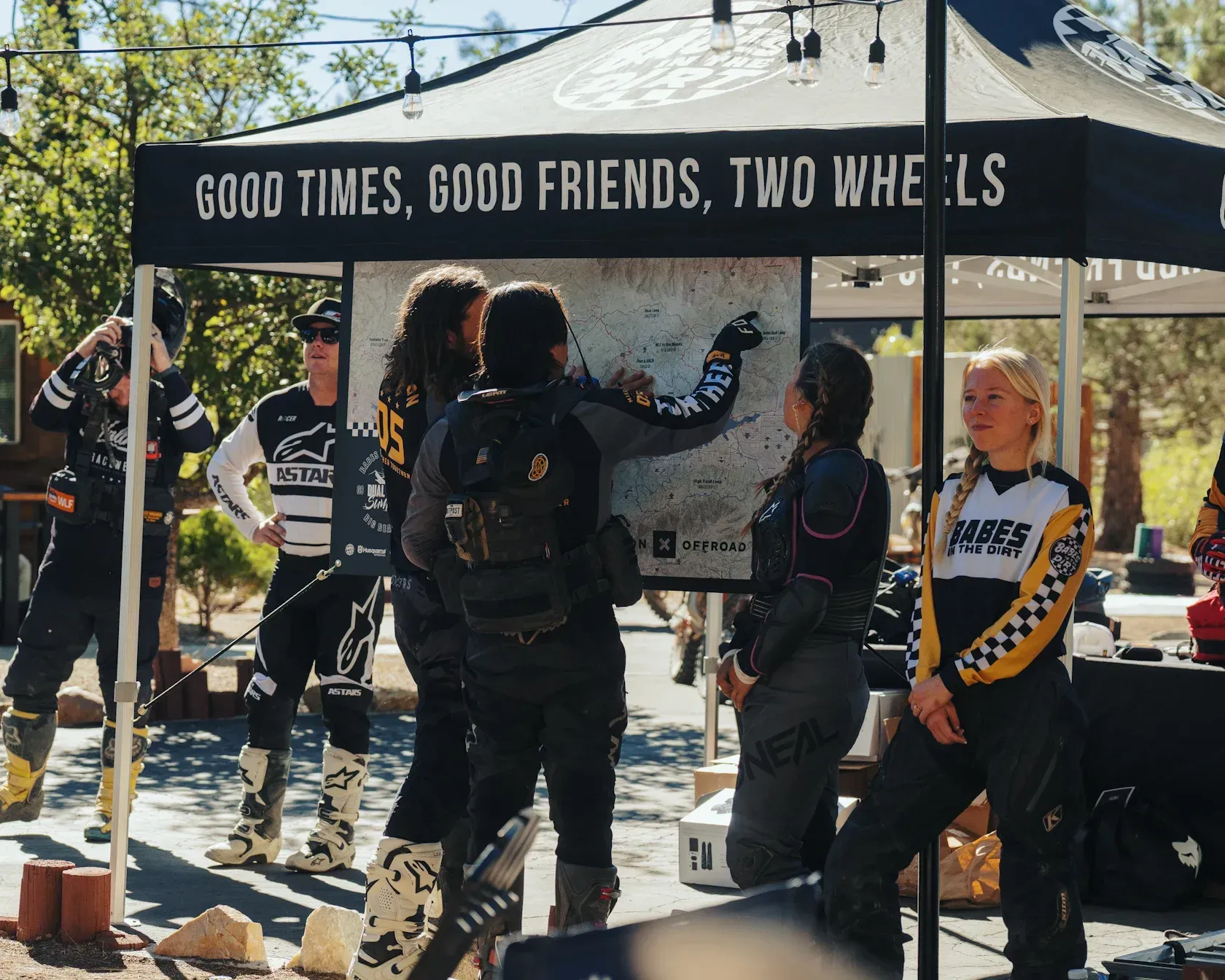Group of people in motorcycle gear looking at a map under a tent that reads 