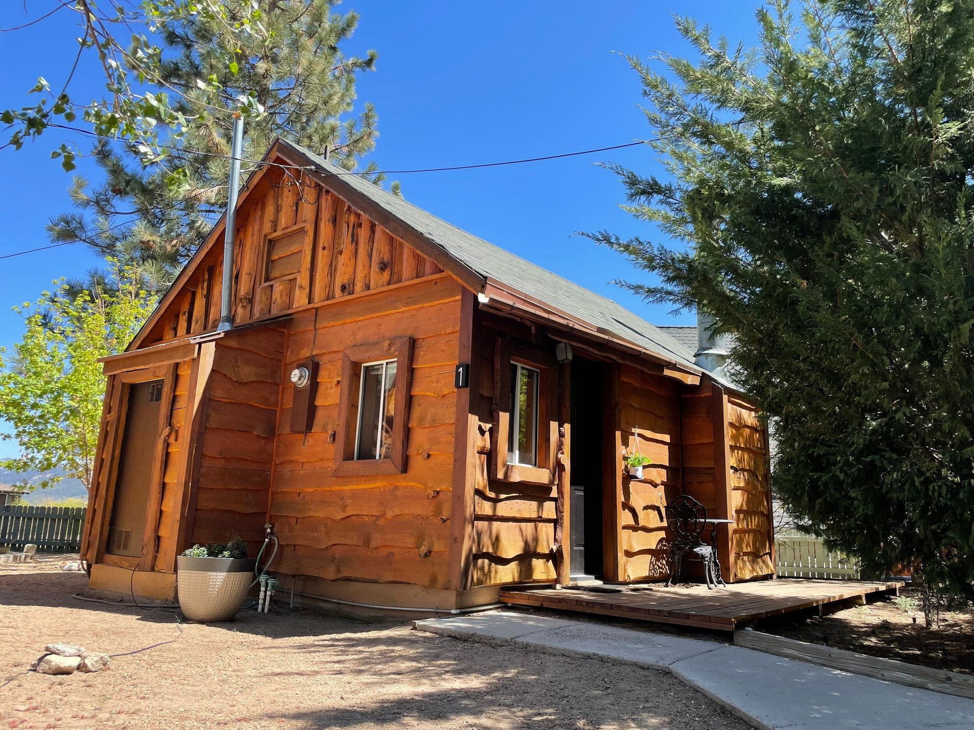 Wooden cabin with brown exterior and small deck, set against a blue sky, surrounded by small plants.