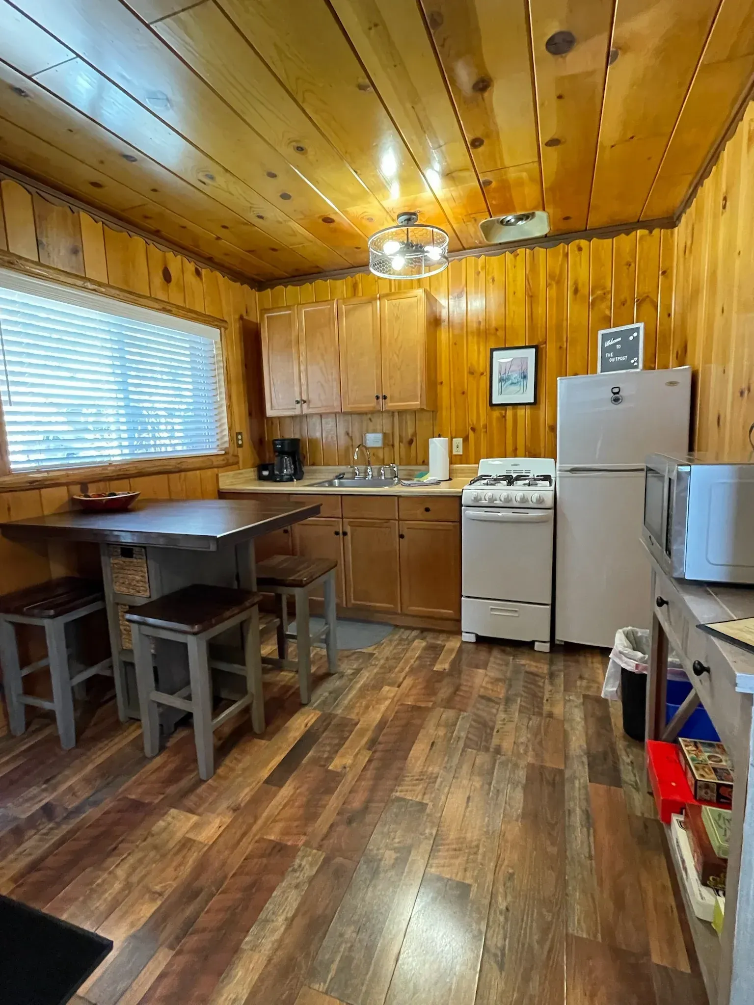 Cozy cabin kitchen with wood paneling, appliances, table and stools.