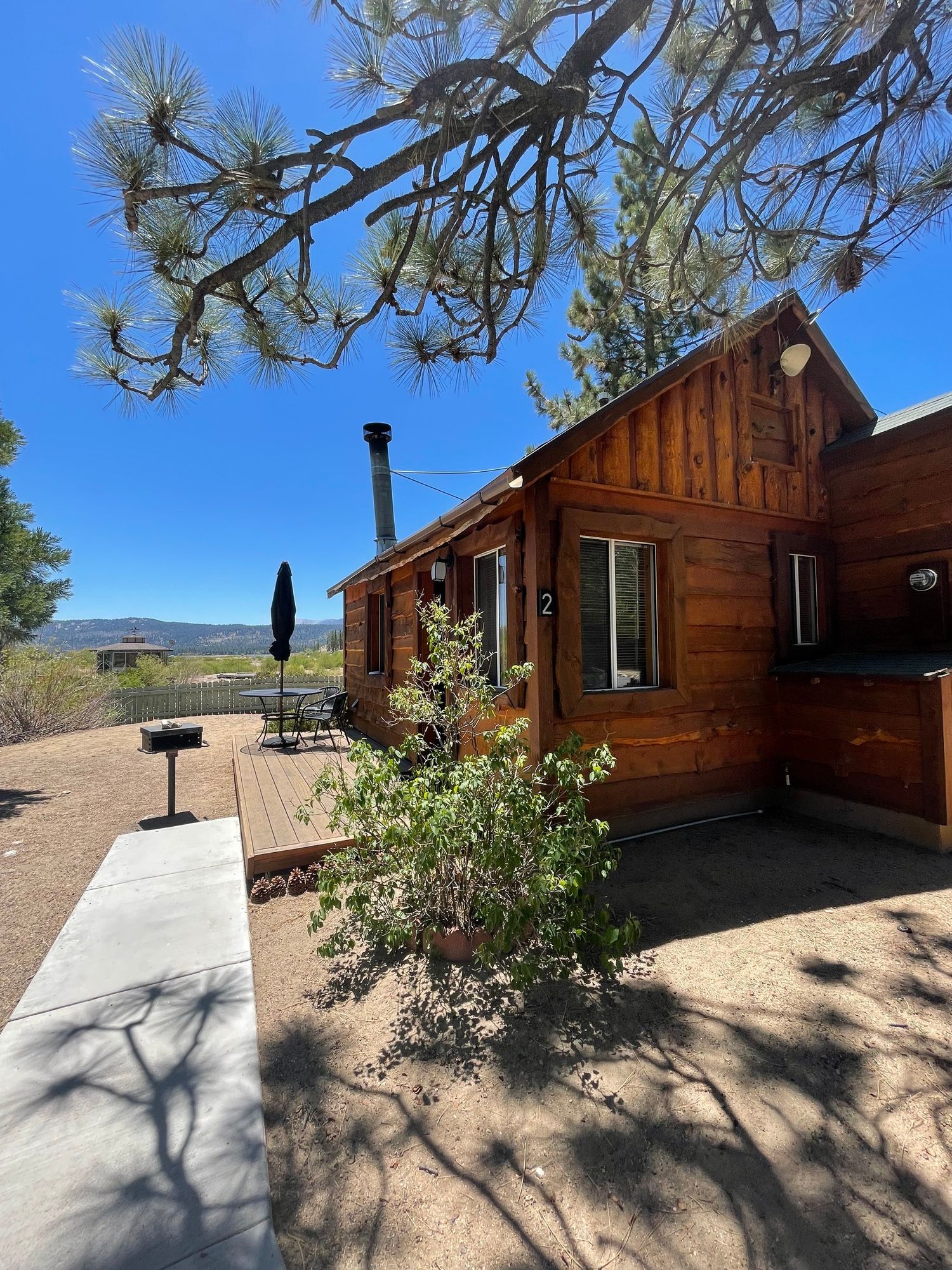 Wooden cabin with a dark chimney and a concrete walkway, sunny day.
