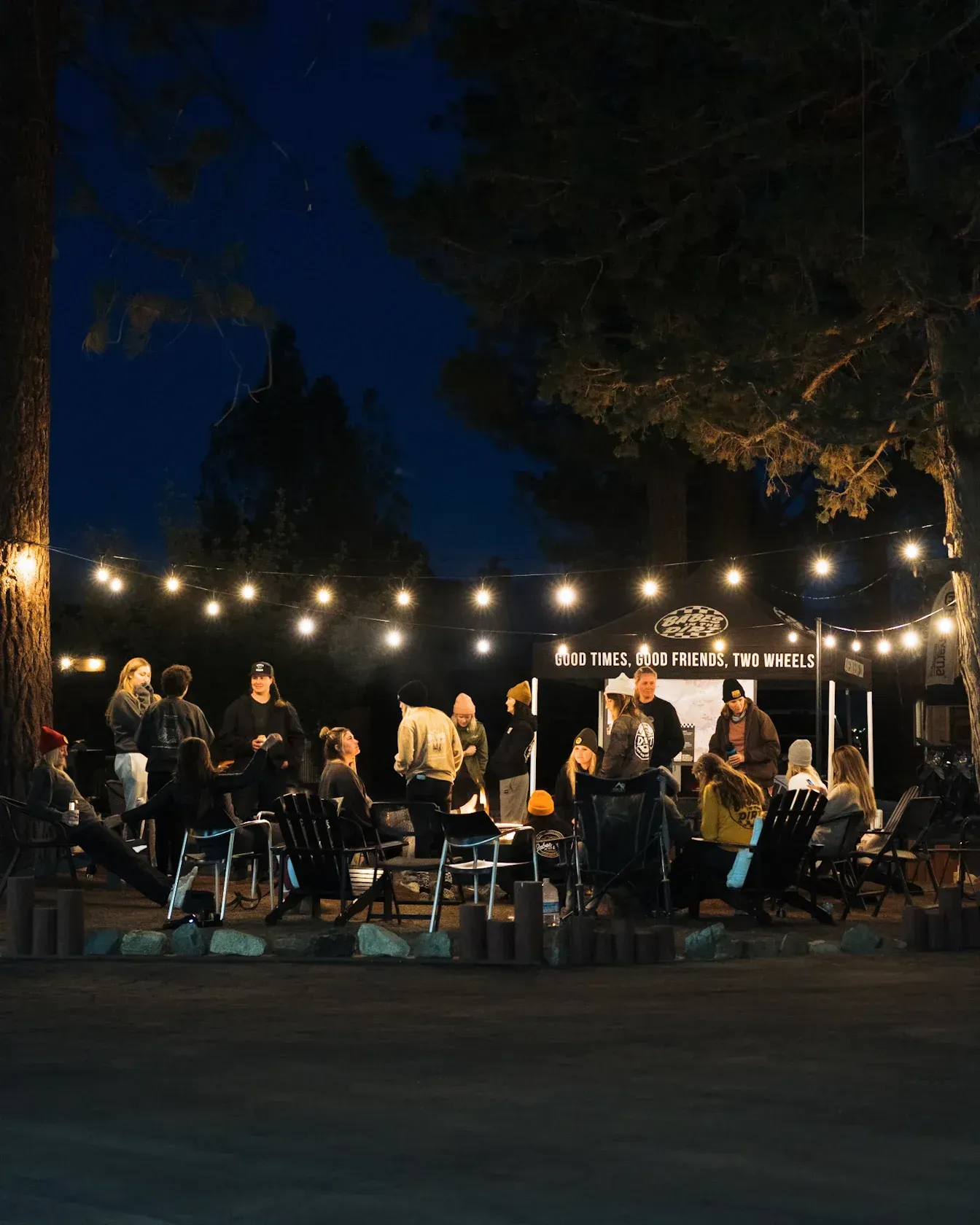 Nighttime outdoor gathering with a group of people, under string lights, near a tent.