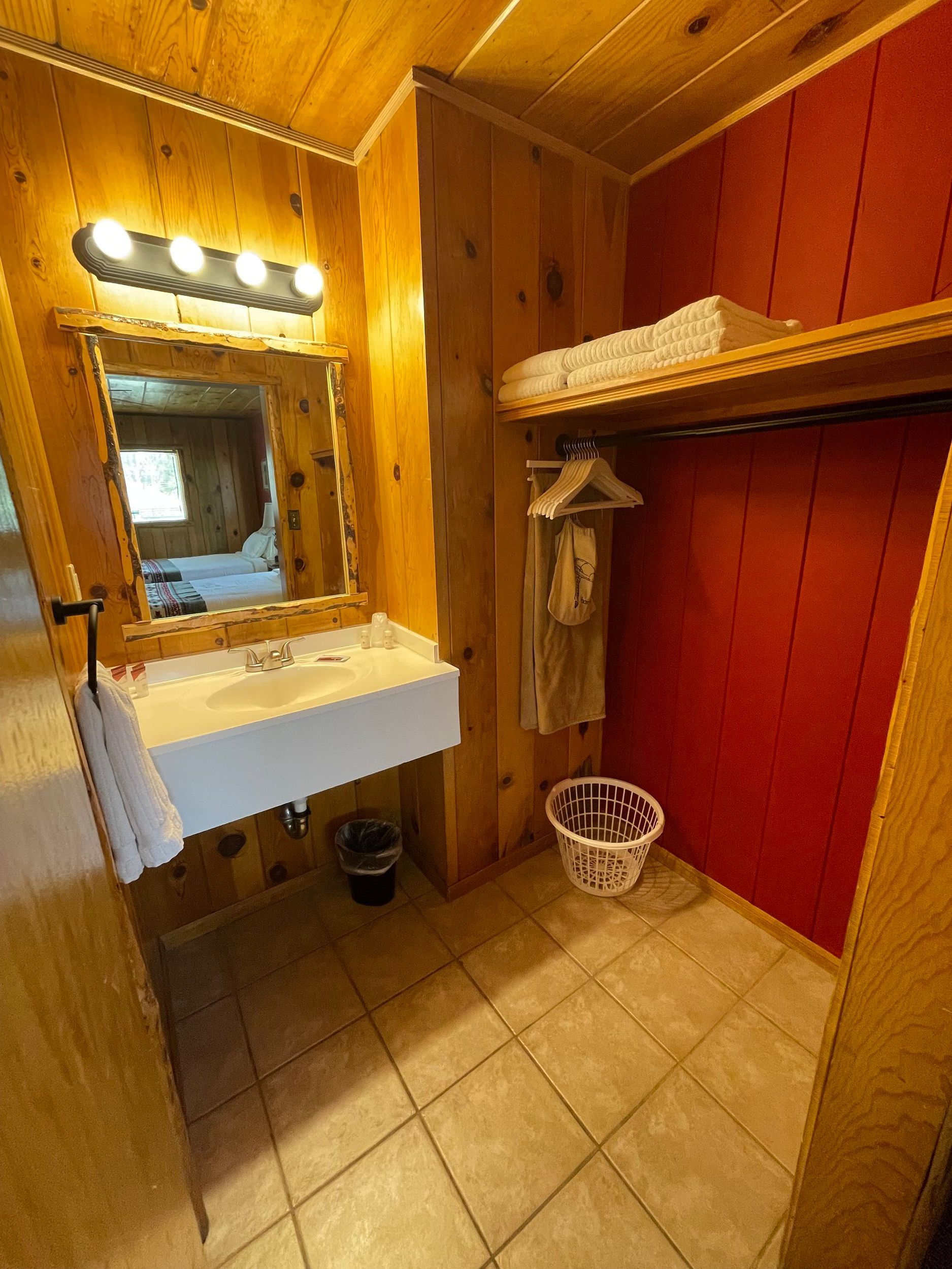 Bathroom with wooden paneling, a sink with mirror, and a closet with a rack.