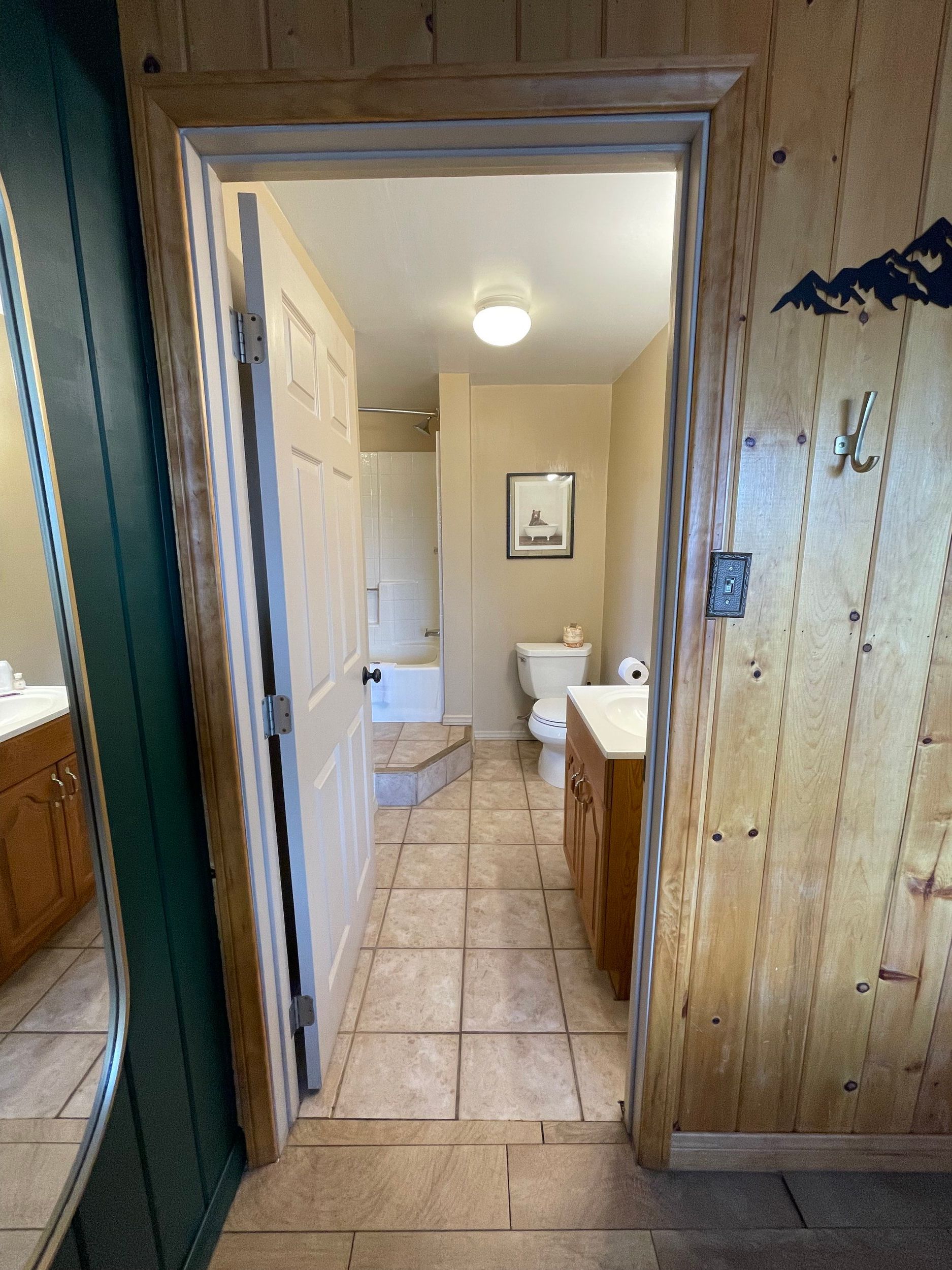 Bathroom doorway with tan tile floor, toilet, vanity, and a framed picture.