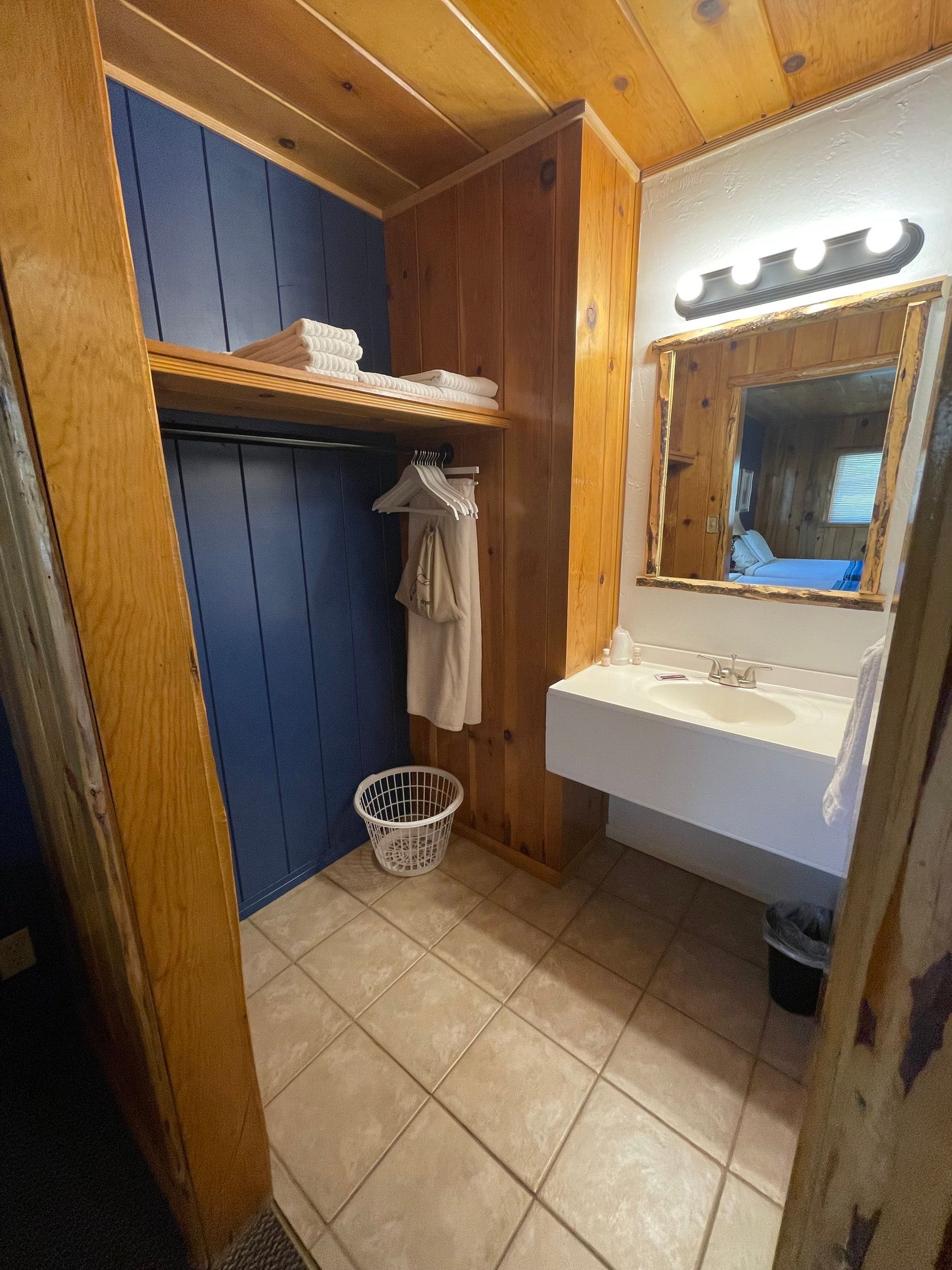 Bathroom with a closet, sink, mirror, and wooden paneling.