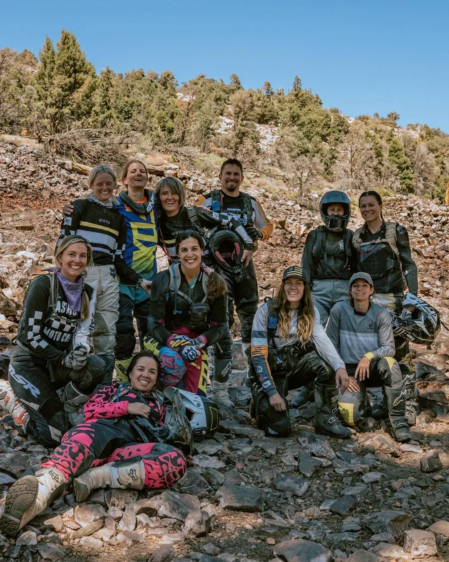 Group of dirt bike riders posing on a rocky trail in the mountains.