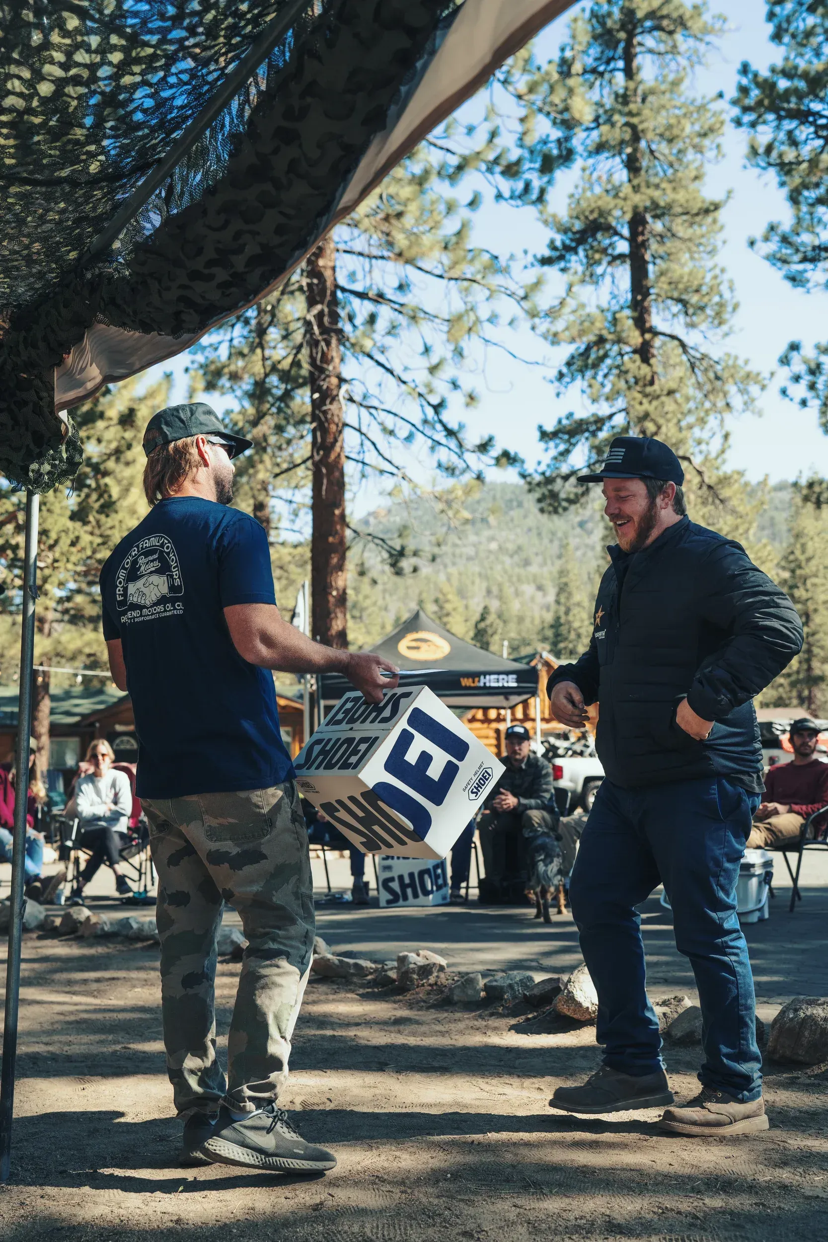 Two men outdoors, one holding a box labeled 