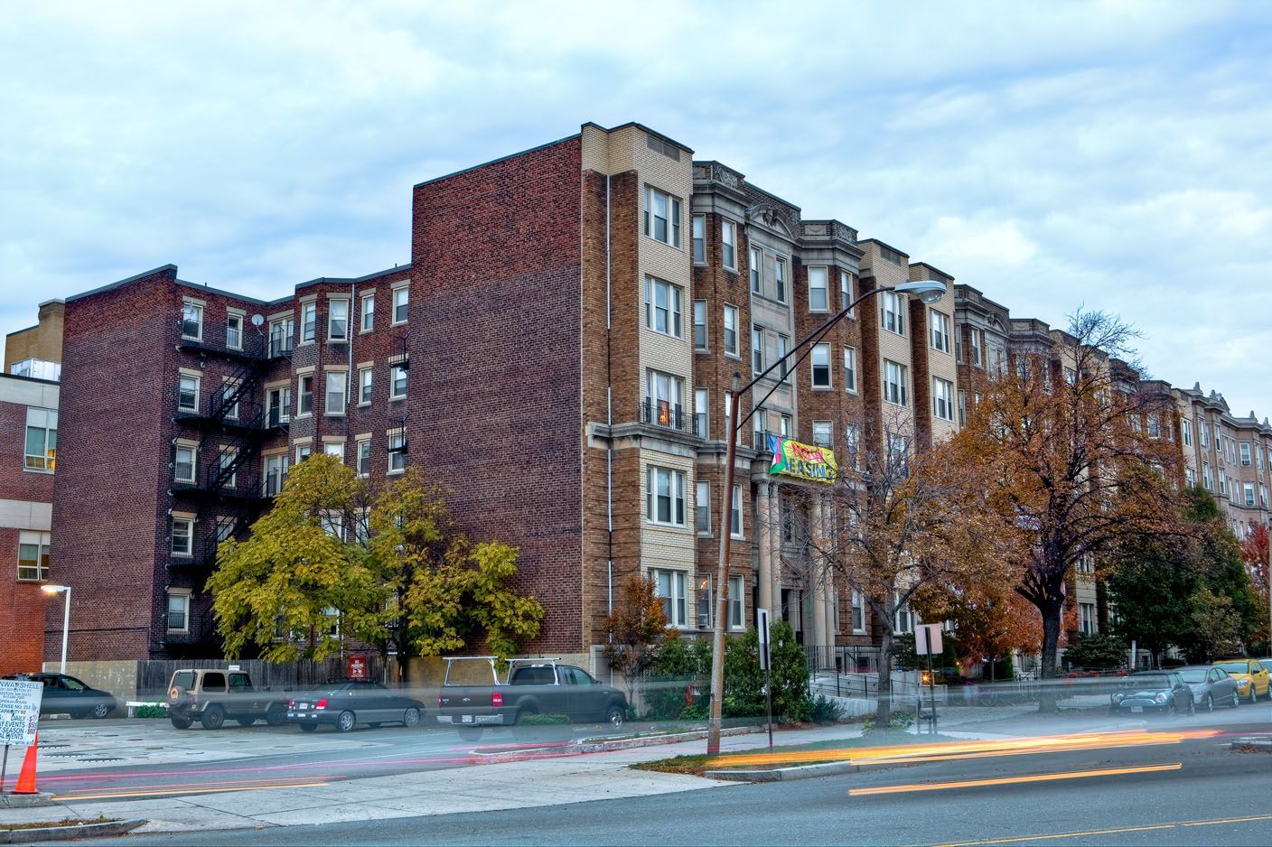 Multi-story brick apartment building on a cloudy day; street level with trees and parked vehicles.