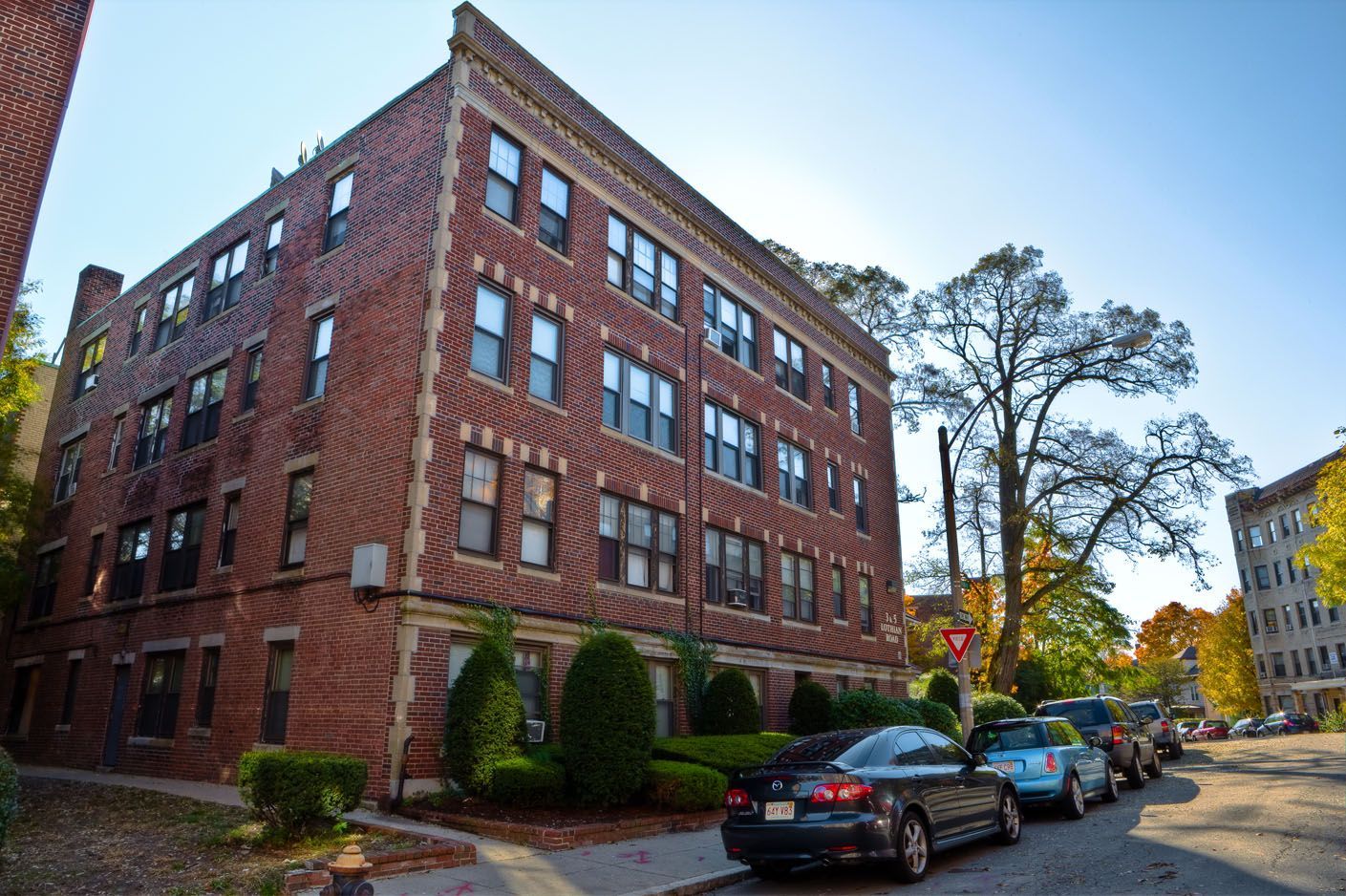 Red brick apartment building with parked cars on a sunny street.