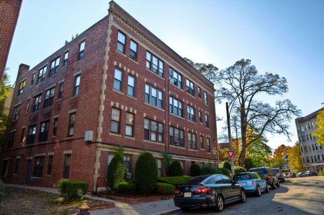 Red brick apartment building with parked cars on a sunny street.