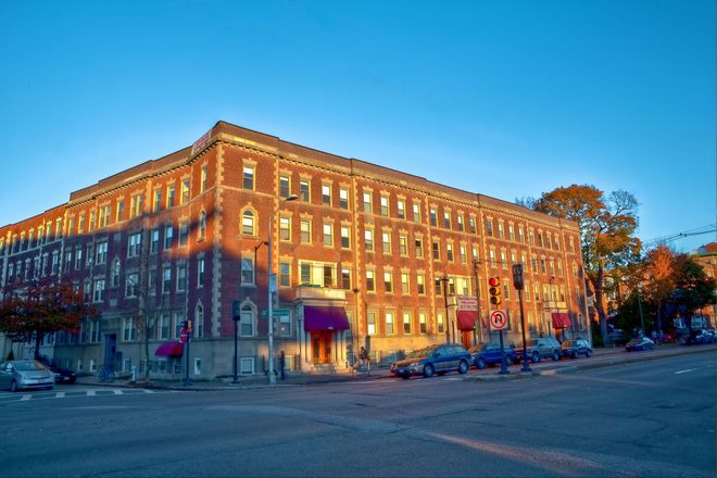 Brick building at sunset with blue sky, corner view. Cars and trees on street.