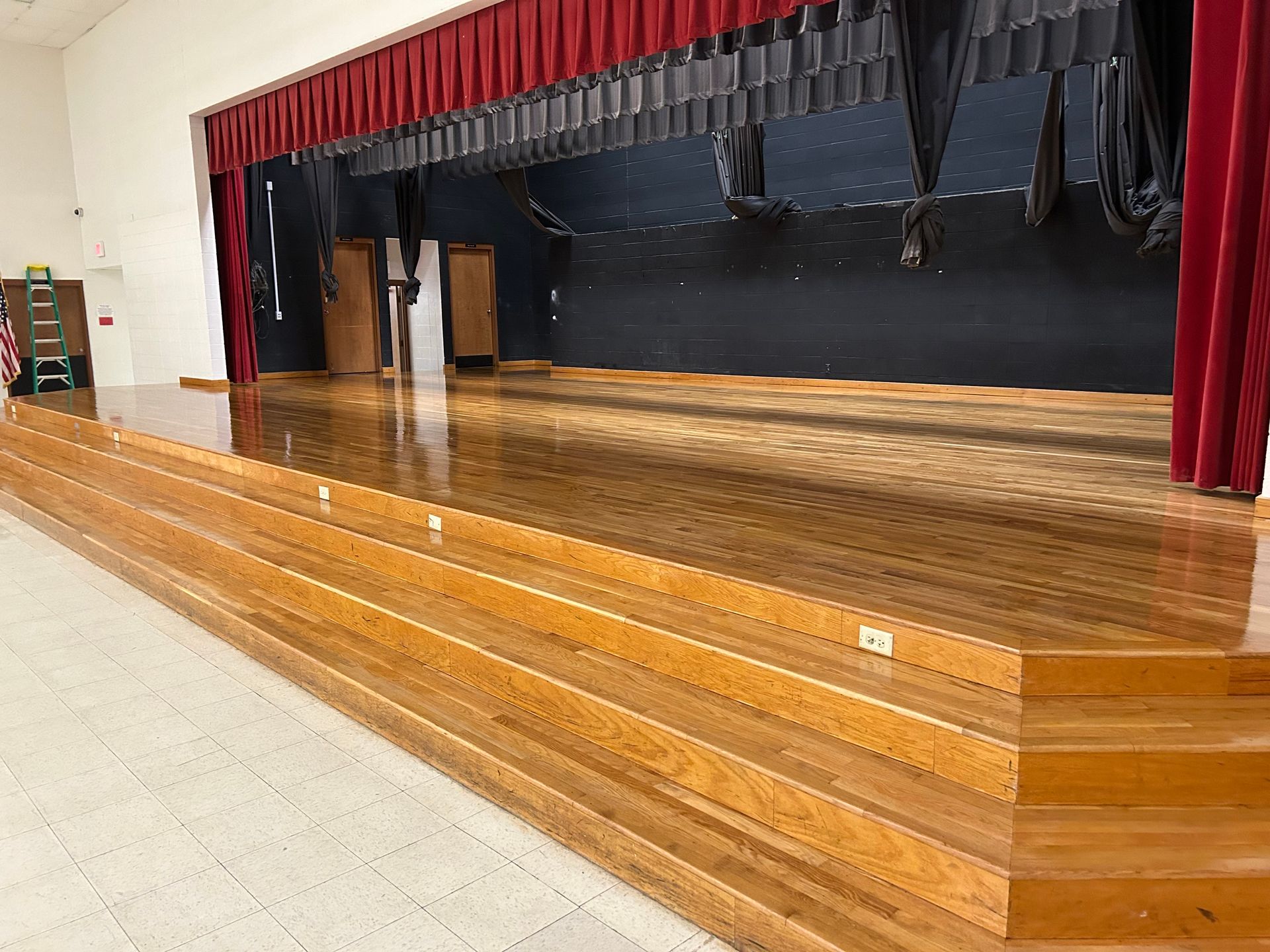 An empty stage with wooden steps and a red curtain.