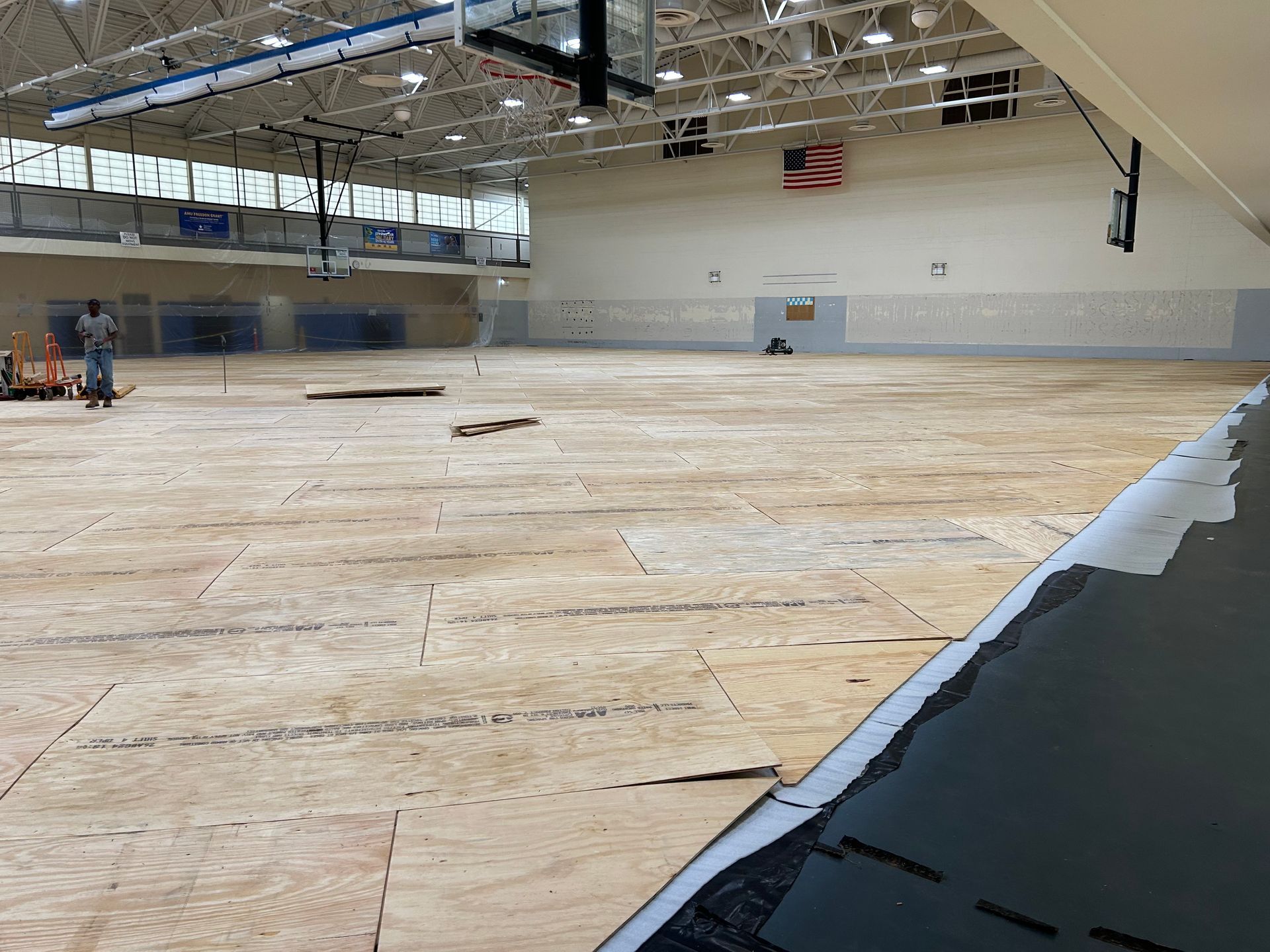 A large empty gym with a wooden floor and a basketball hoop.
