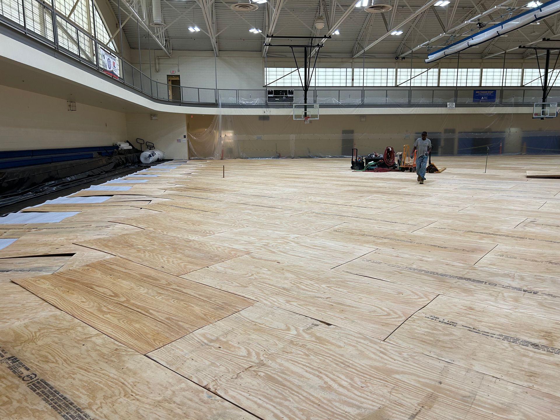 A large empty gym with a wooden floor and a basketball hoop.