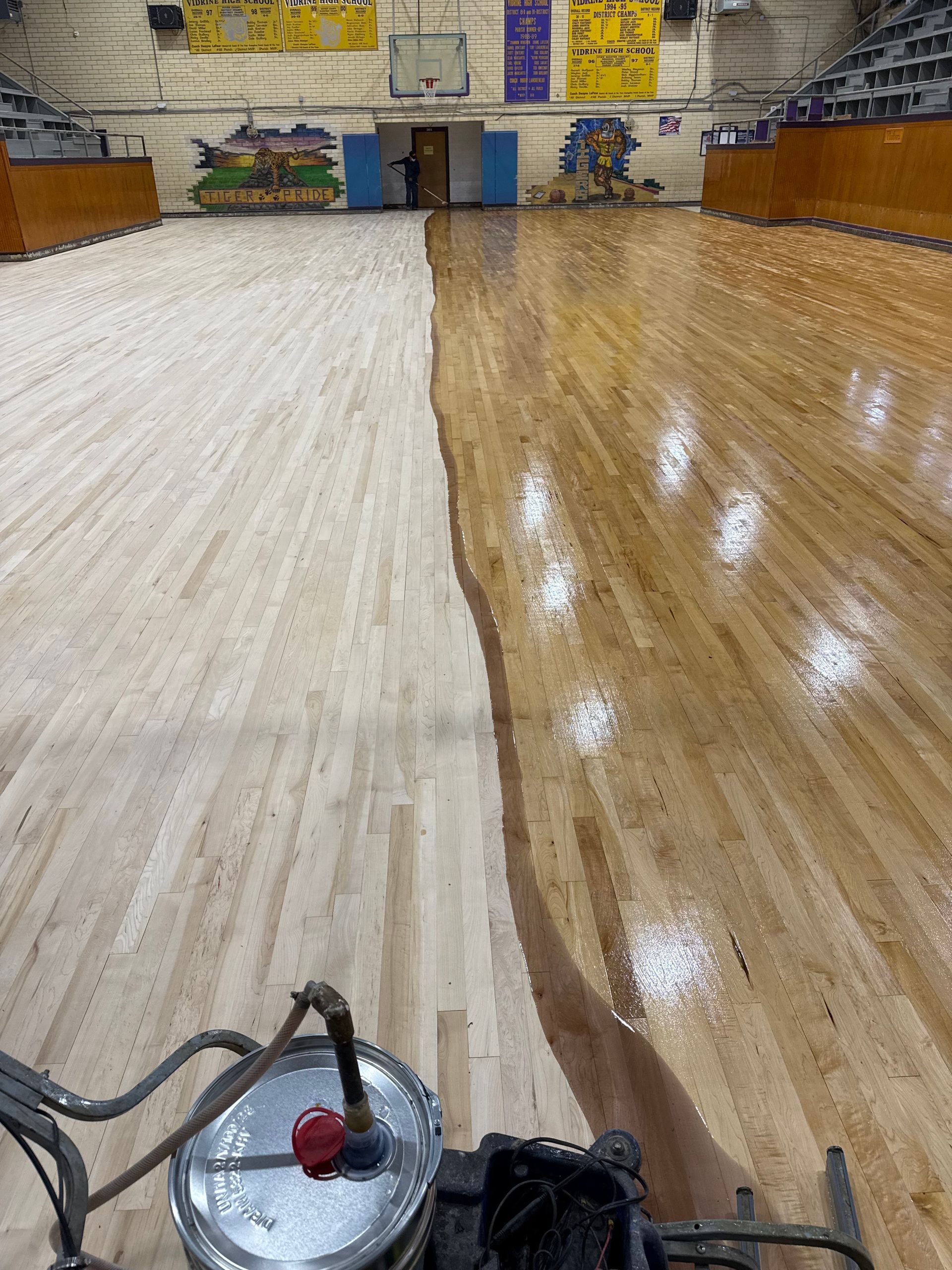 A person is painting a wooden floor in a gym.