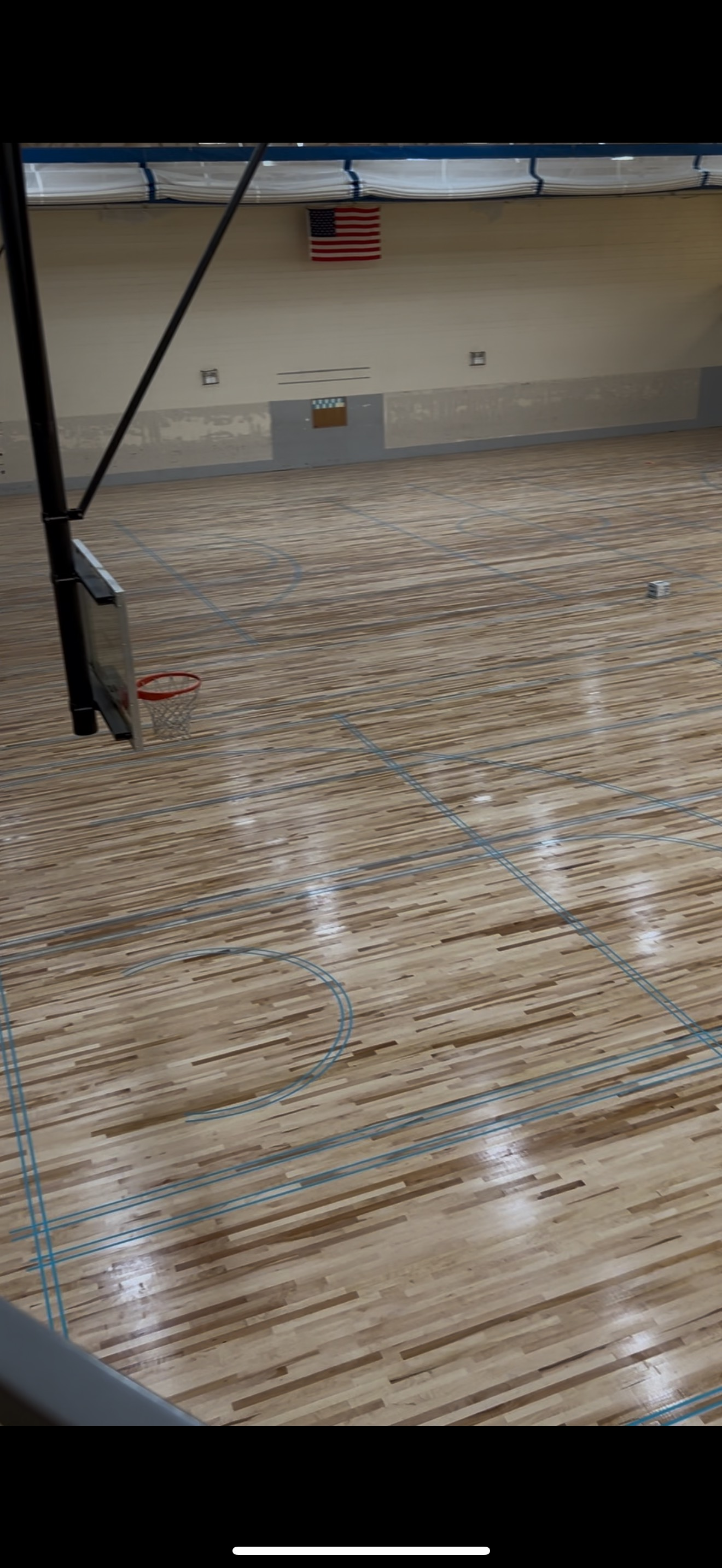 A basketball court with a wooden floor and an american flag on the wall.