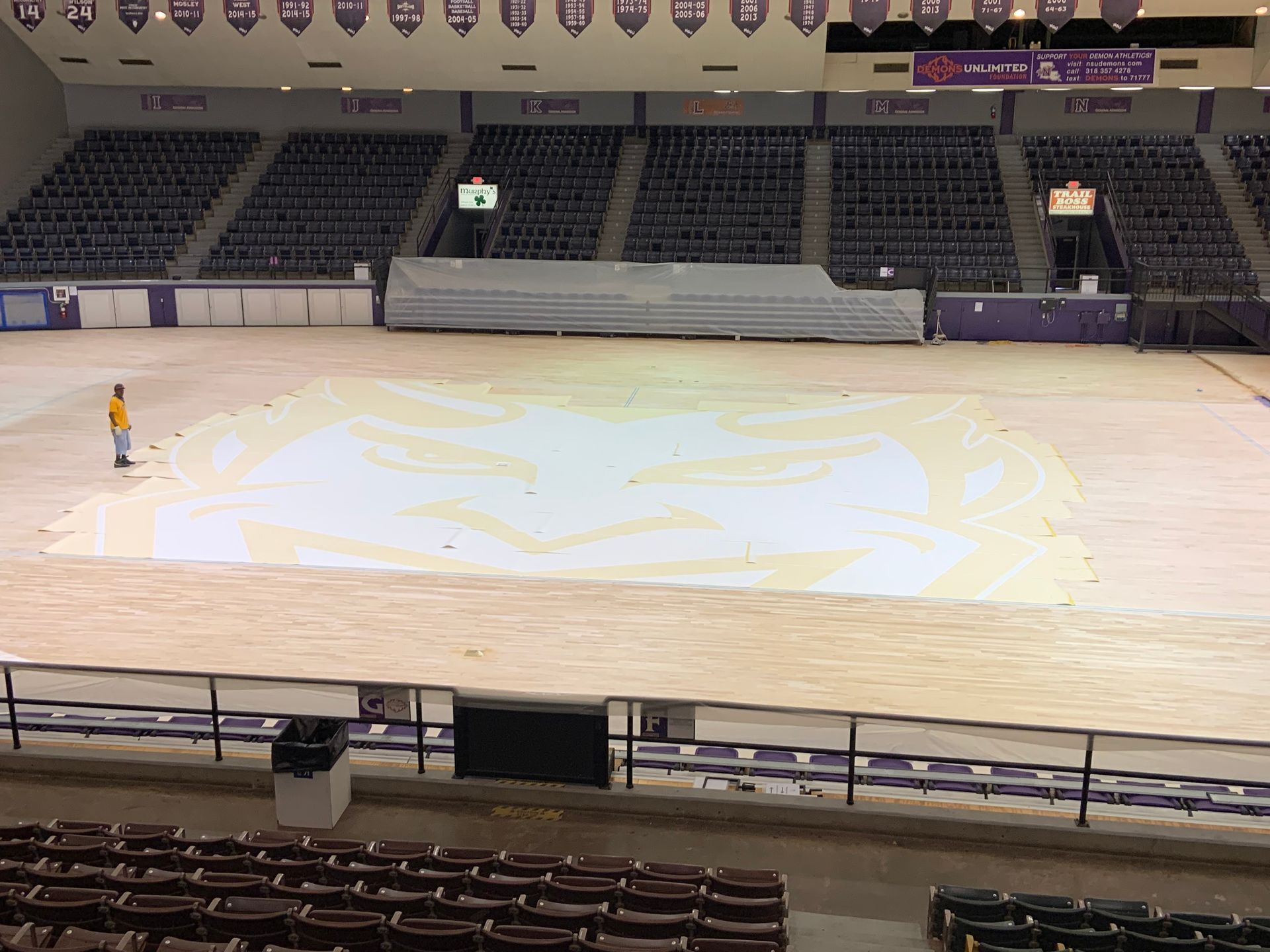 A man in an orange shirt is standing in an empty stadium
