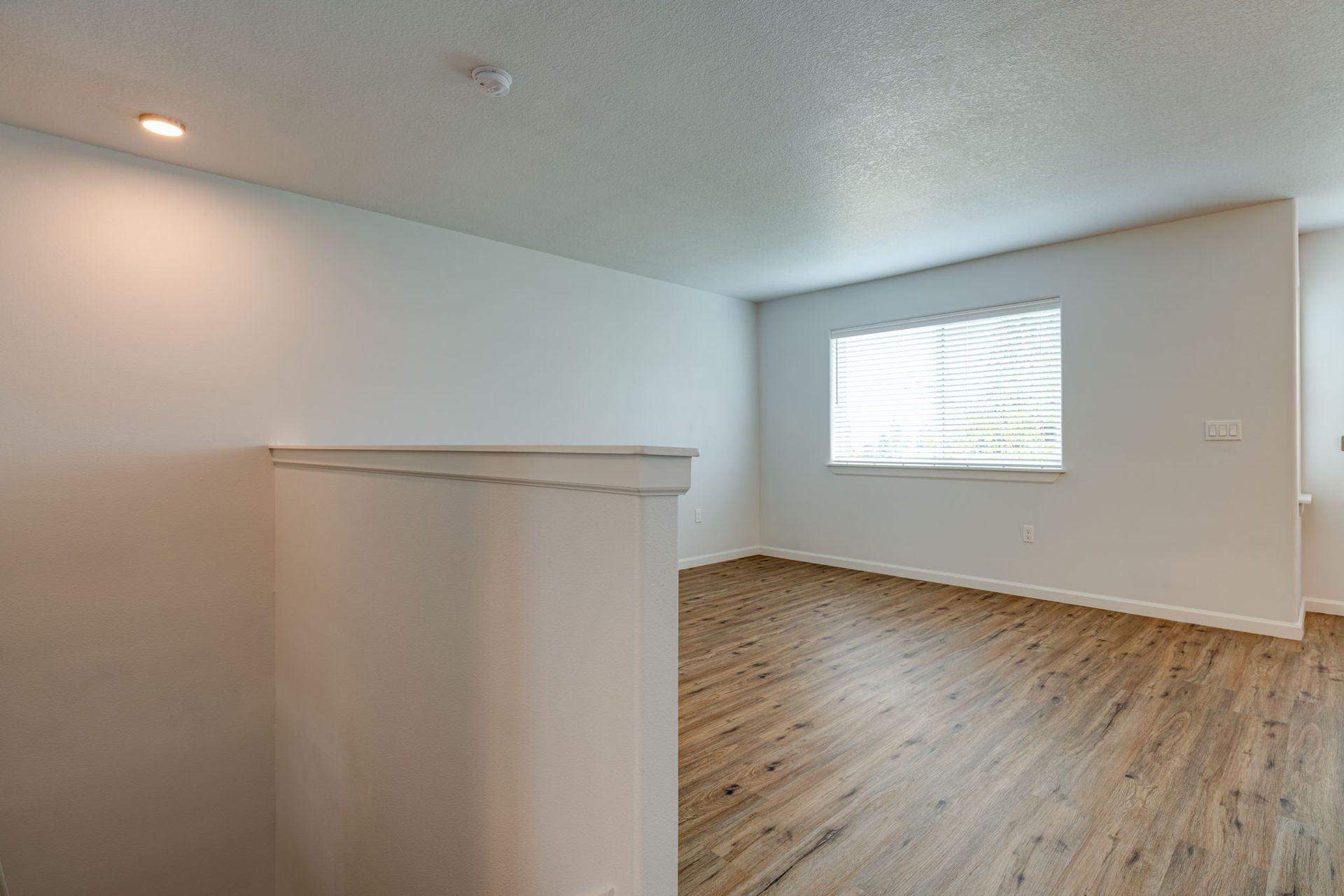 view into unfurnished living room from the top of stairs looking over pony wall