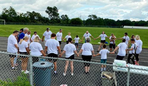 People in white shirts holding hands in a circle on a track field.