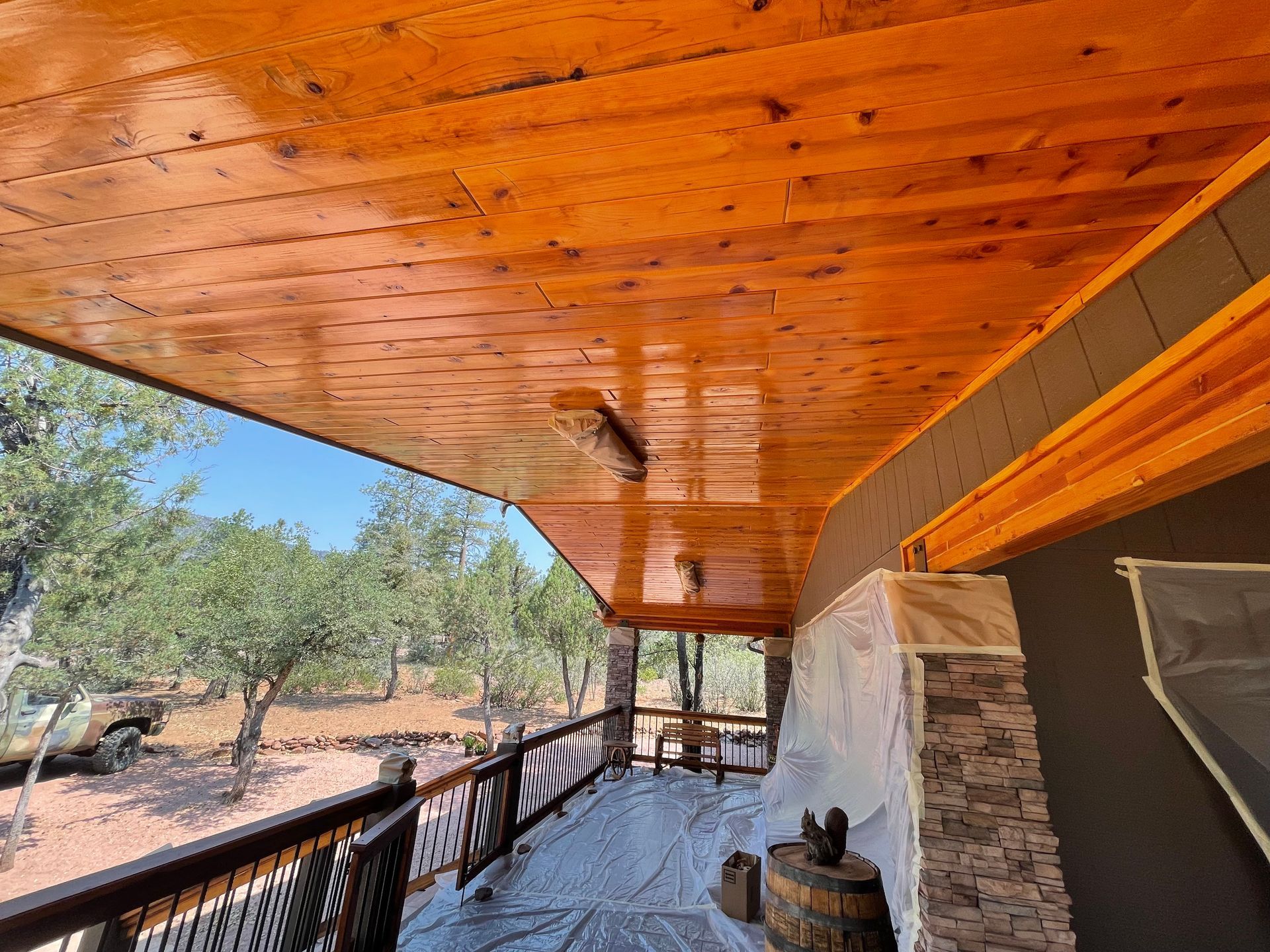 A porch with a wooden ceiling and a view of trees.