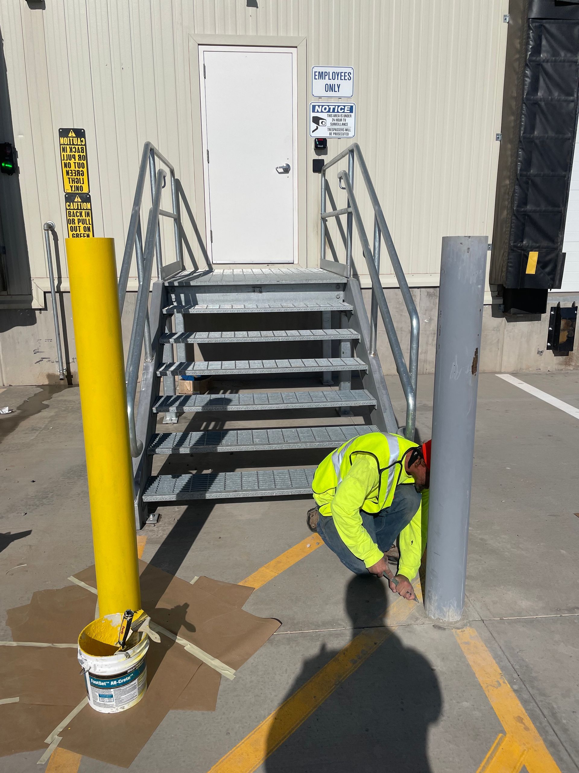 A man is kneeling down next to a yellow pole with a caution sign on it