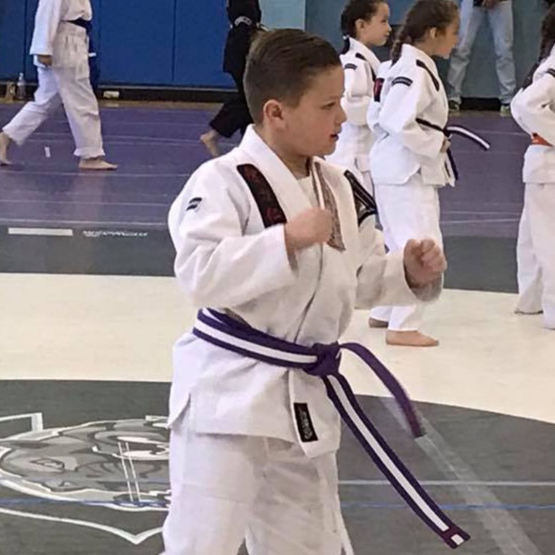 A man is kneeling down next to a young boy in a taekwondo class.