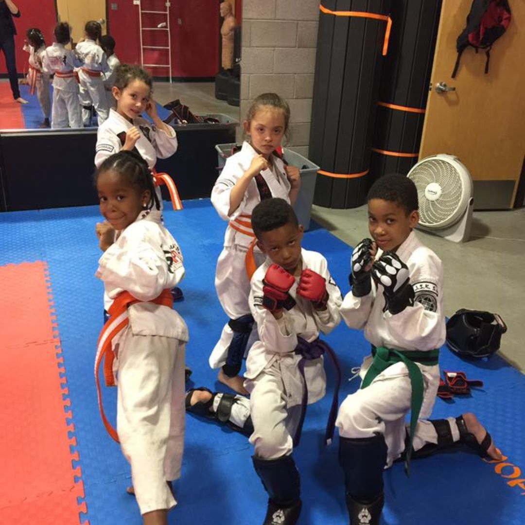 A young girl in a karate uniform is sitting on the floor.