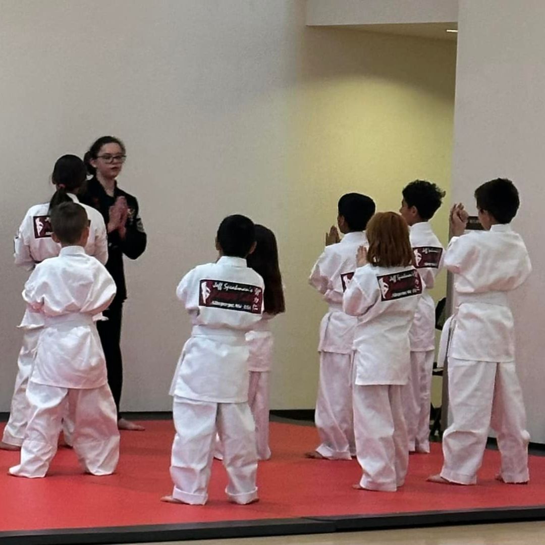 A group of children are practicing karate with a teacher in a gym.