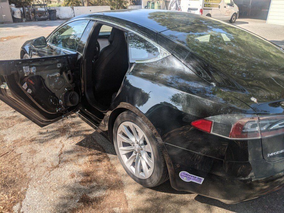 A black tesla model s with its doors open is parked in a parking lot.