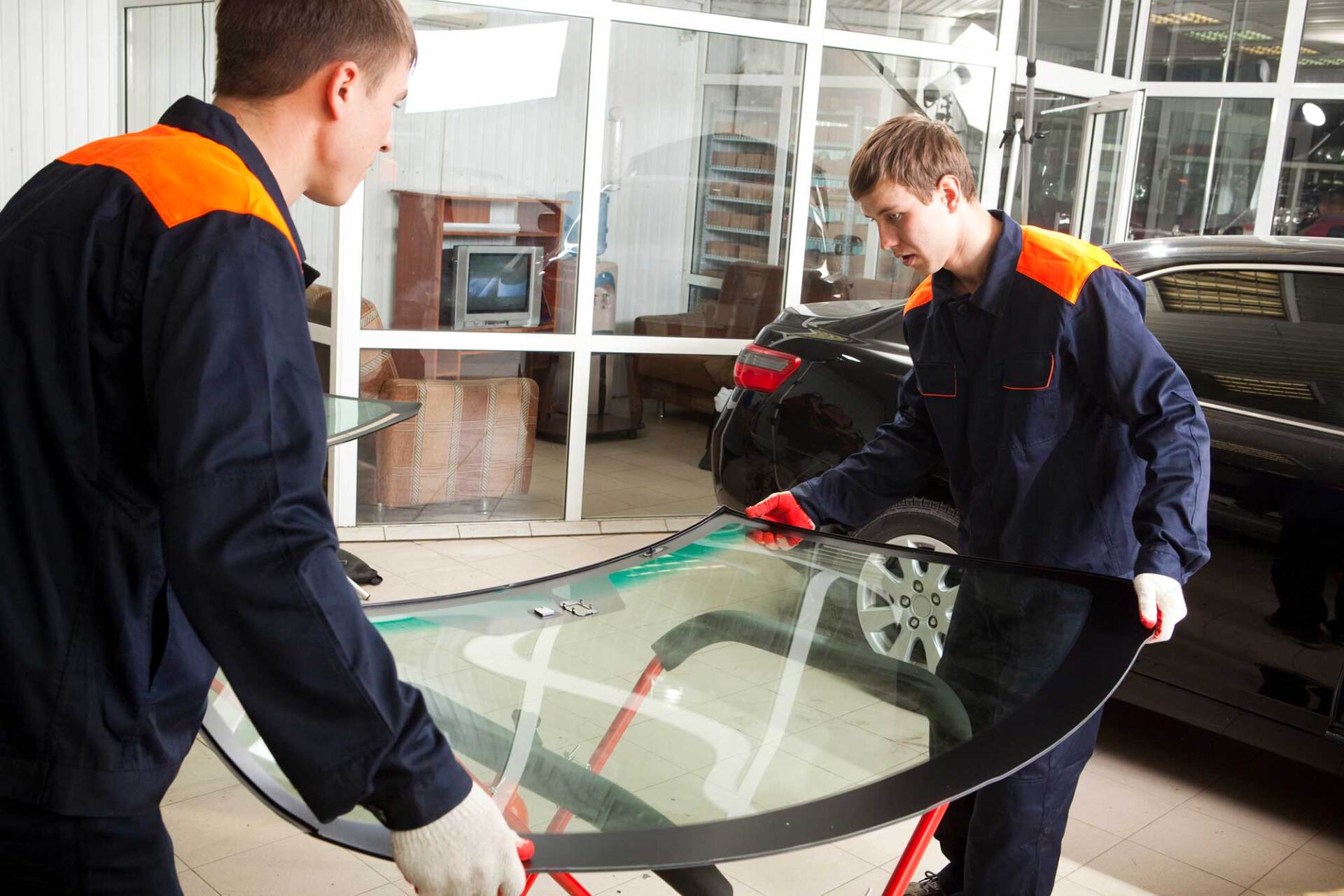 Two men are working on a windshield in a garage.
