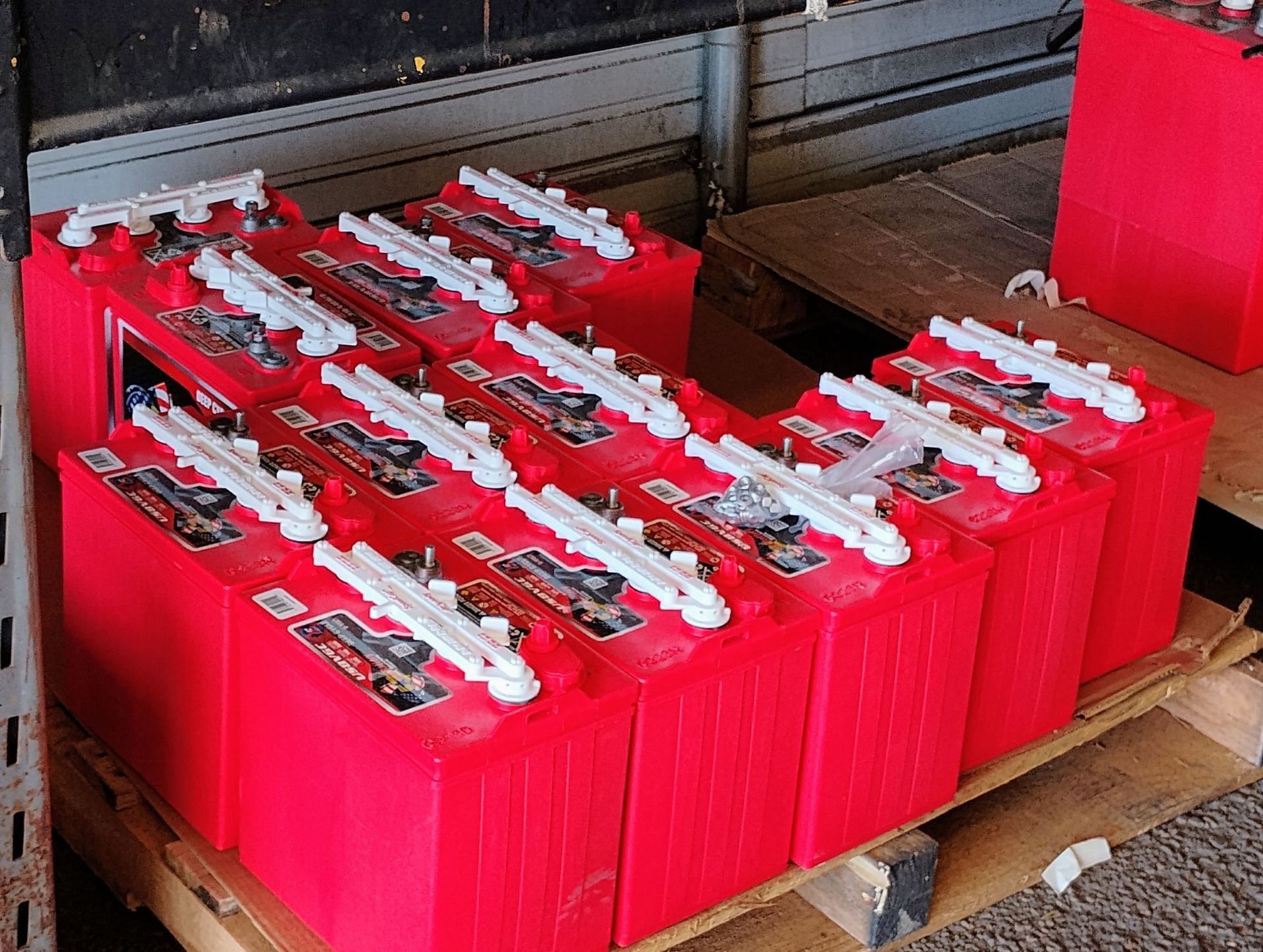 A bunch of red batteries are stacked on top of each other on a wooden pallet.