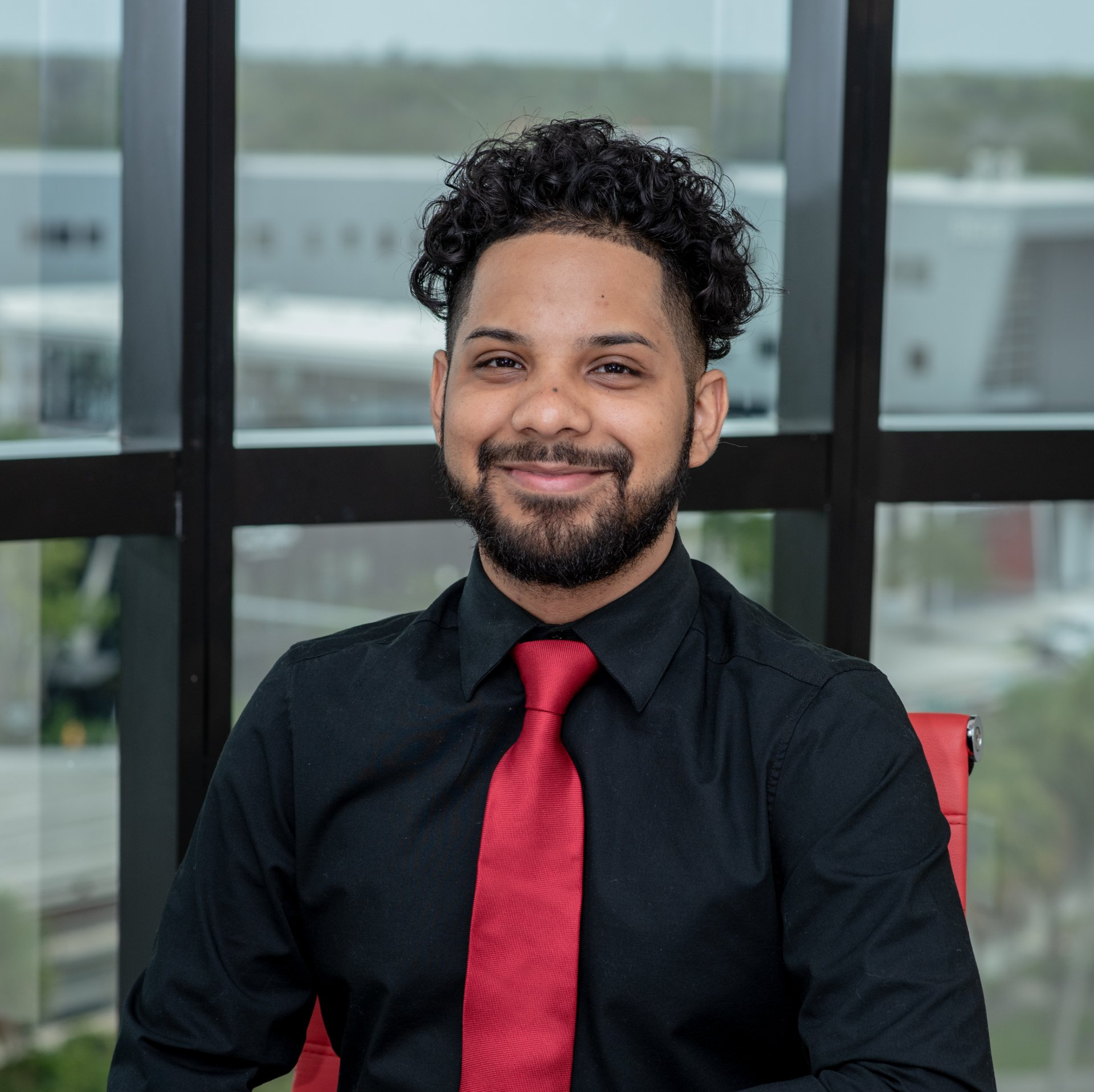 A man with a beard wearing a black shirt and red tie
