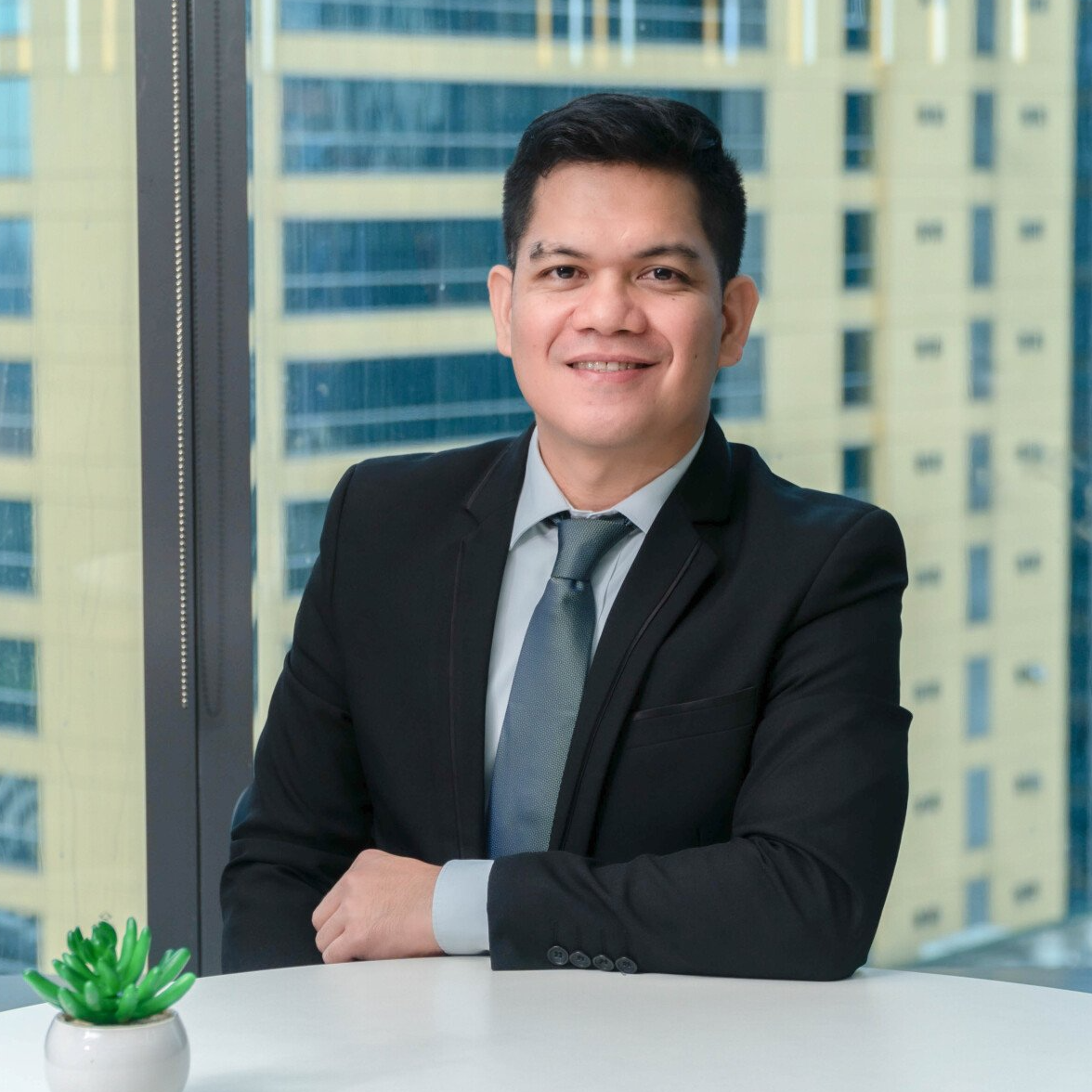 A woman is sitting at a table in front of a window and smiling
